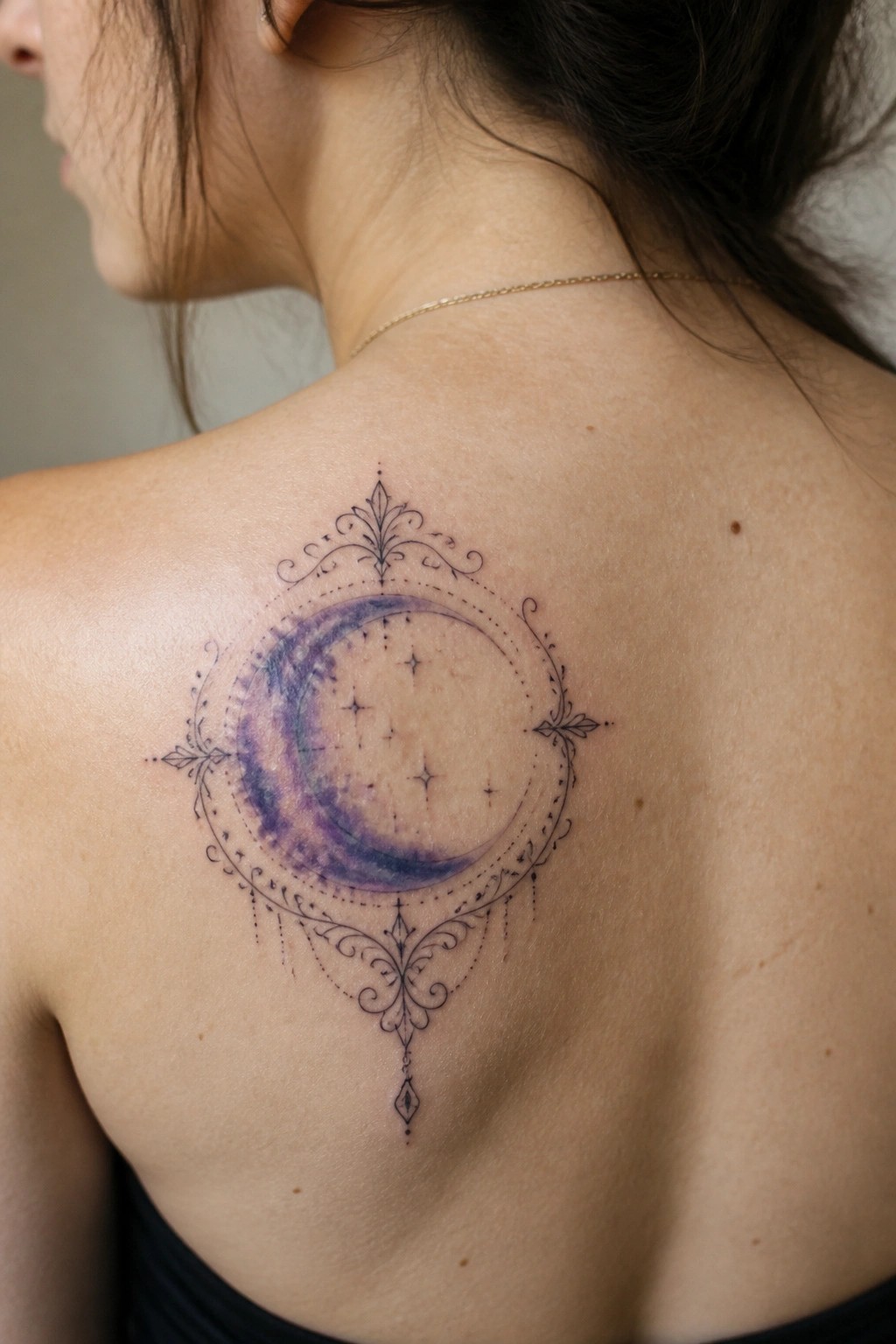 Ornate purple crescent moon tattoo with black filigree and stars on woman's back