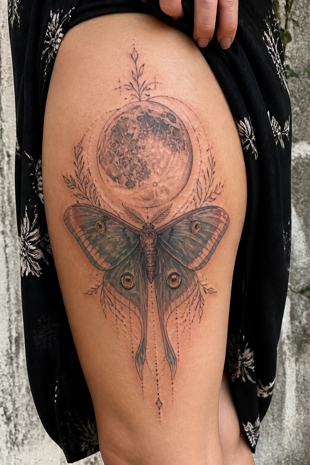 Detailed moth and full moon tattoo on thigh under black floral fabric