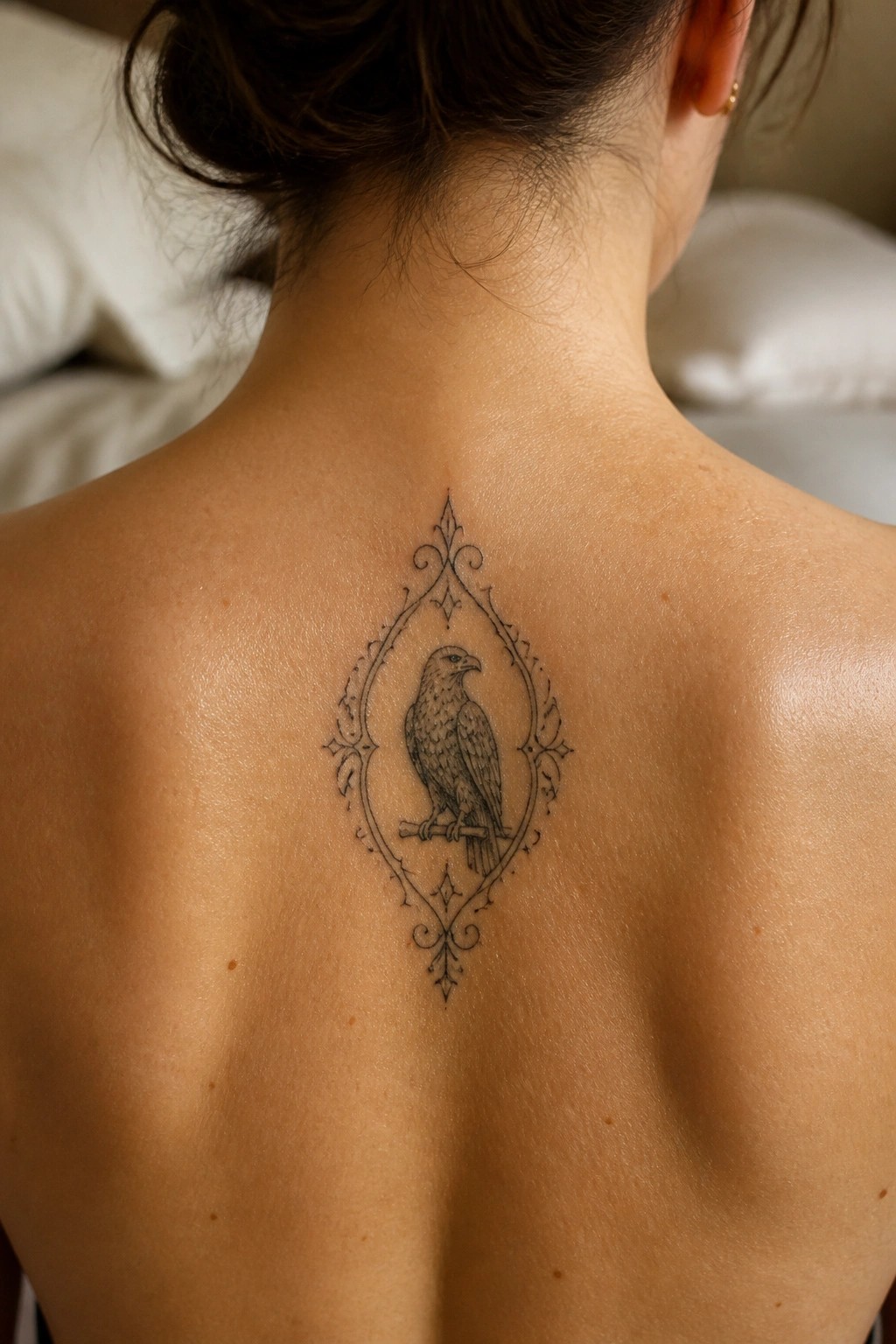 Ornate black ink tattoo of a hawk in decorative frame on upper back