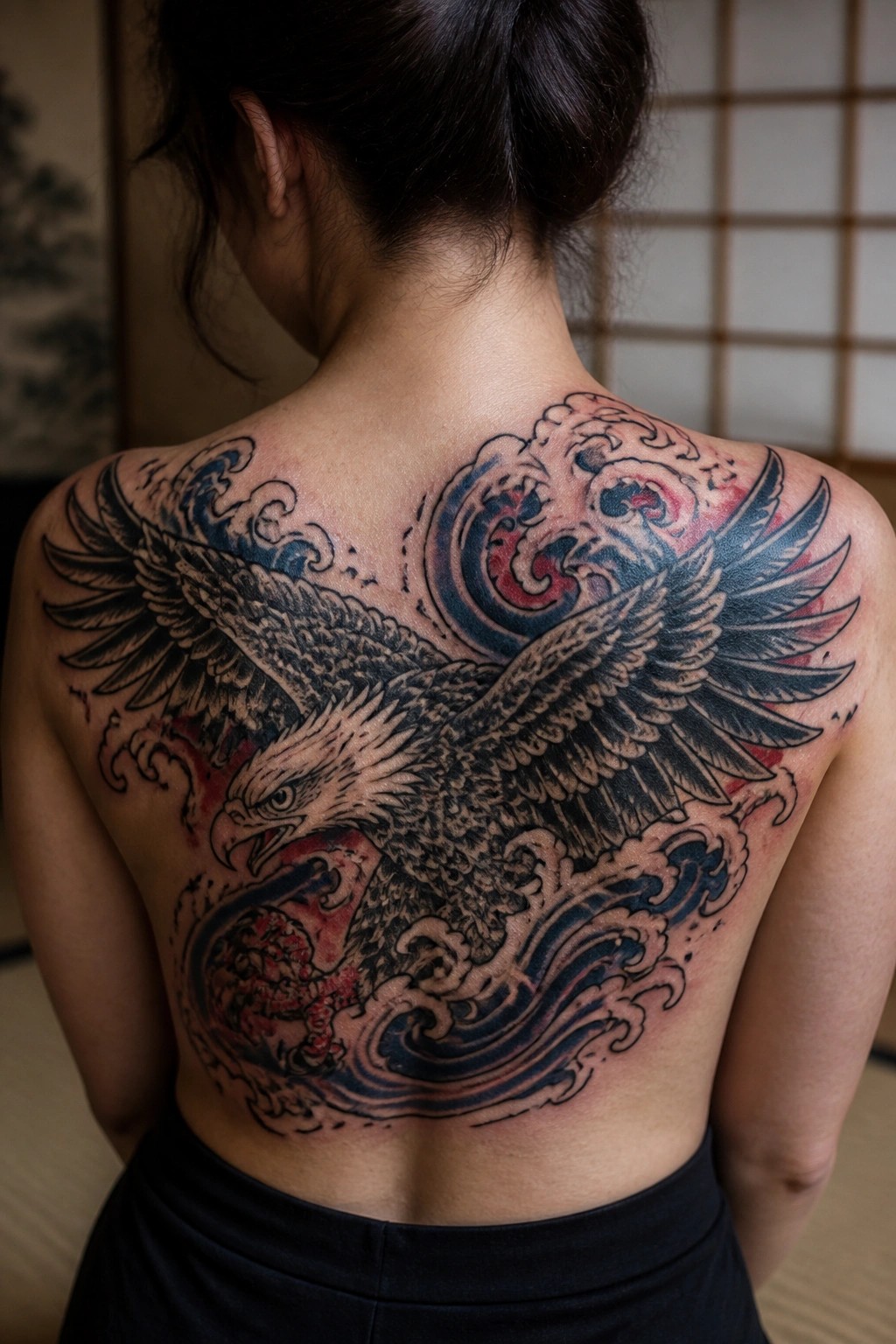 Large traditional Japanese style eagle tattoo across a woman's full back, with wings spread over blue waves and red accents.
