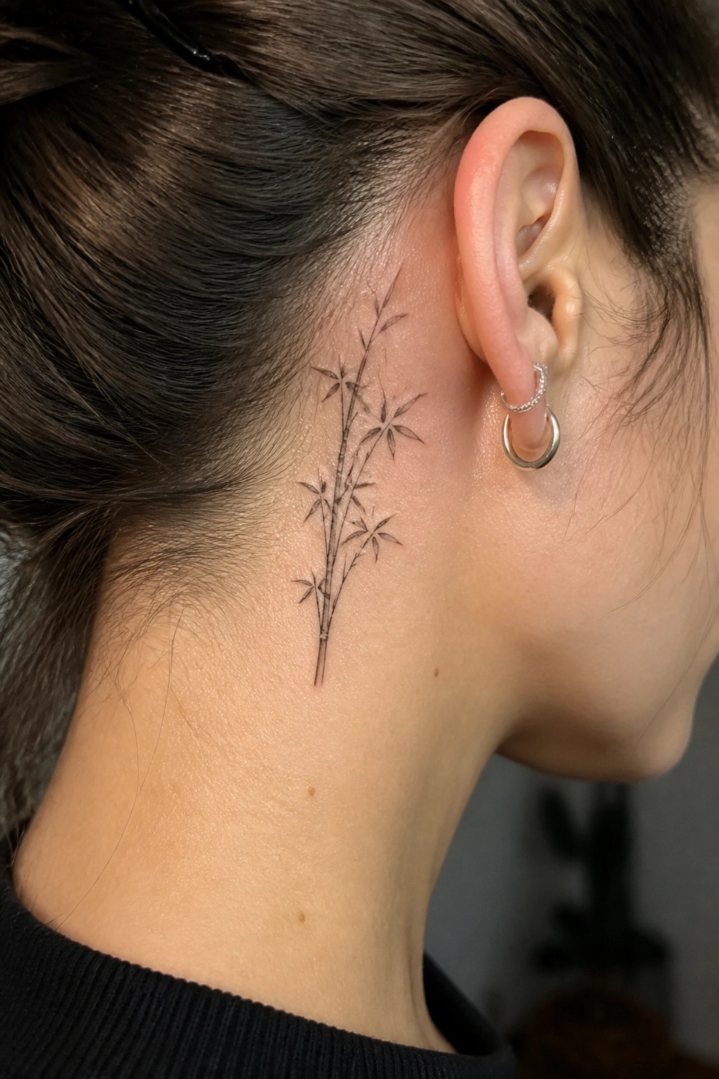 Bamboo tattoo behind ear on neck with dark hair and hoop earrings