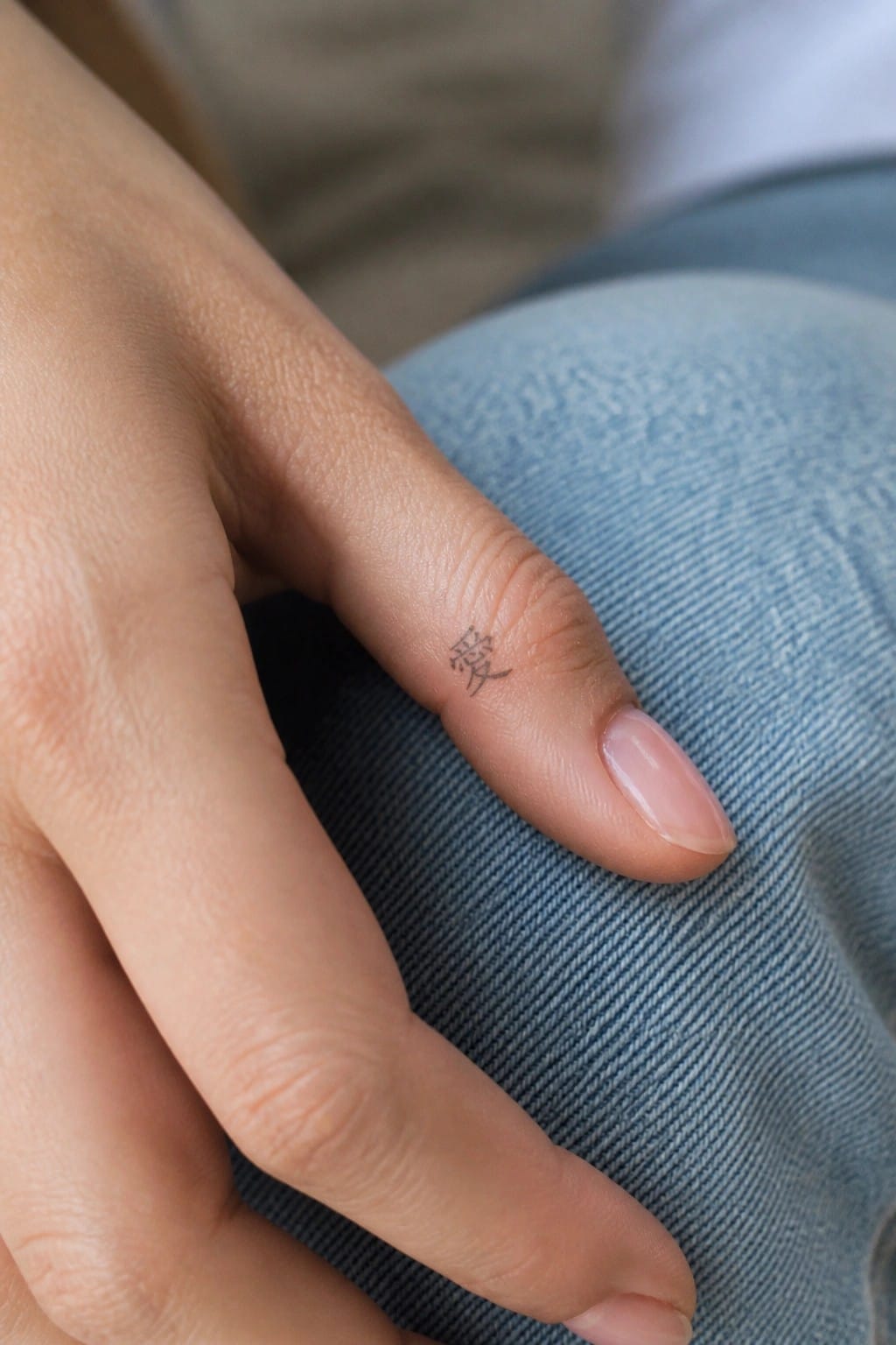 Hand with small Chinese character tattoo on index finger resting on blue denim.