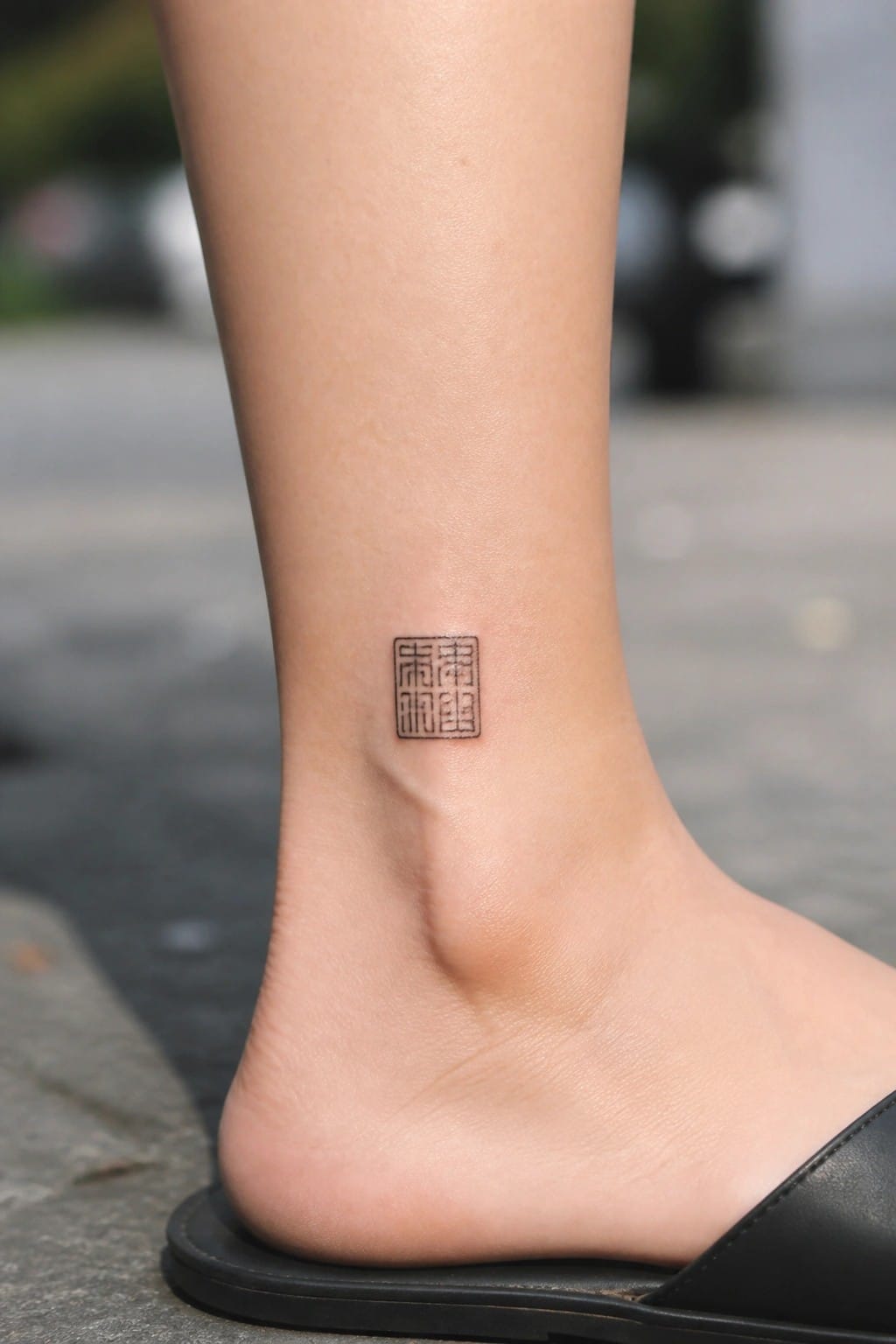 Small fine line Chinese seal tattoo with four characters on a woman's ankle.