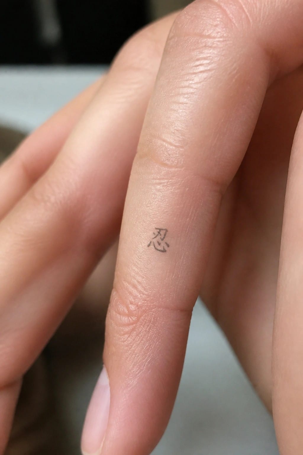 Small black Chinese character tattoo on the side of a finger