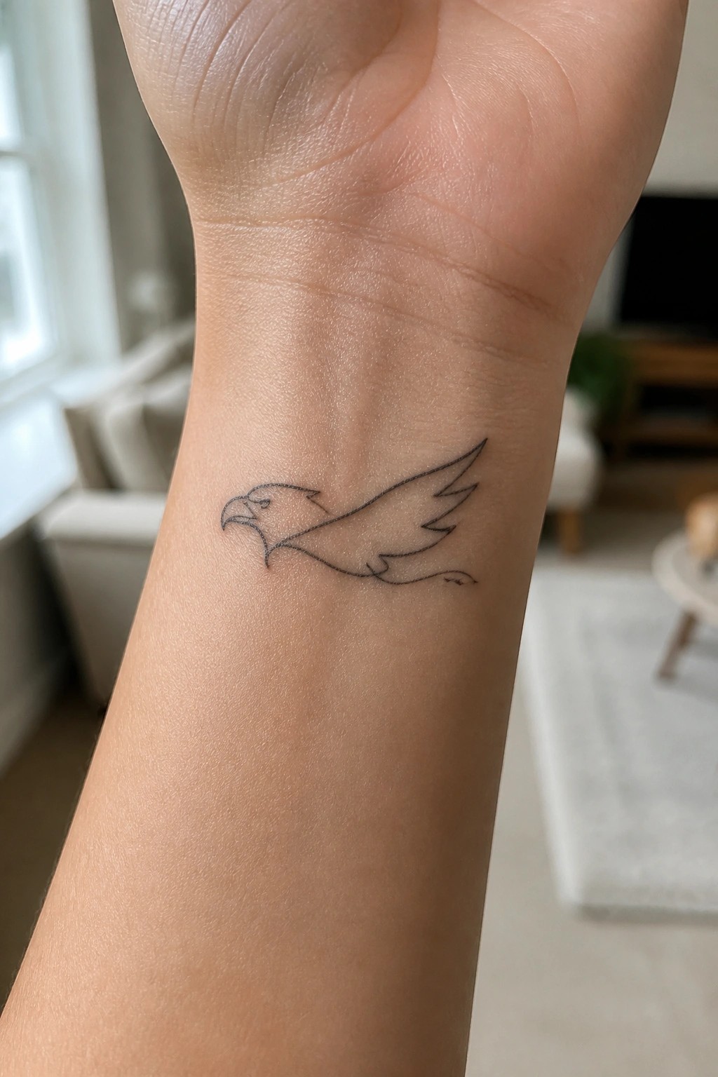 Minimalist black line tattoo of a flying eagle on light-skinned wrist