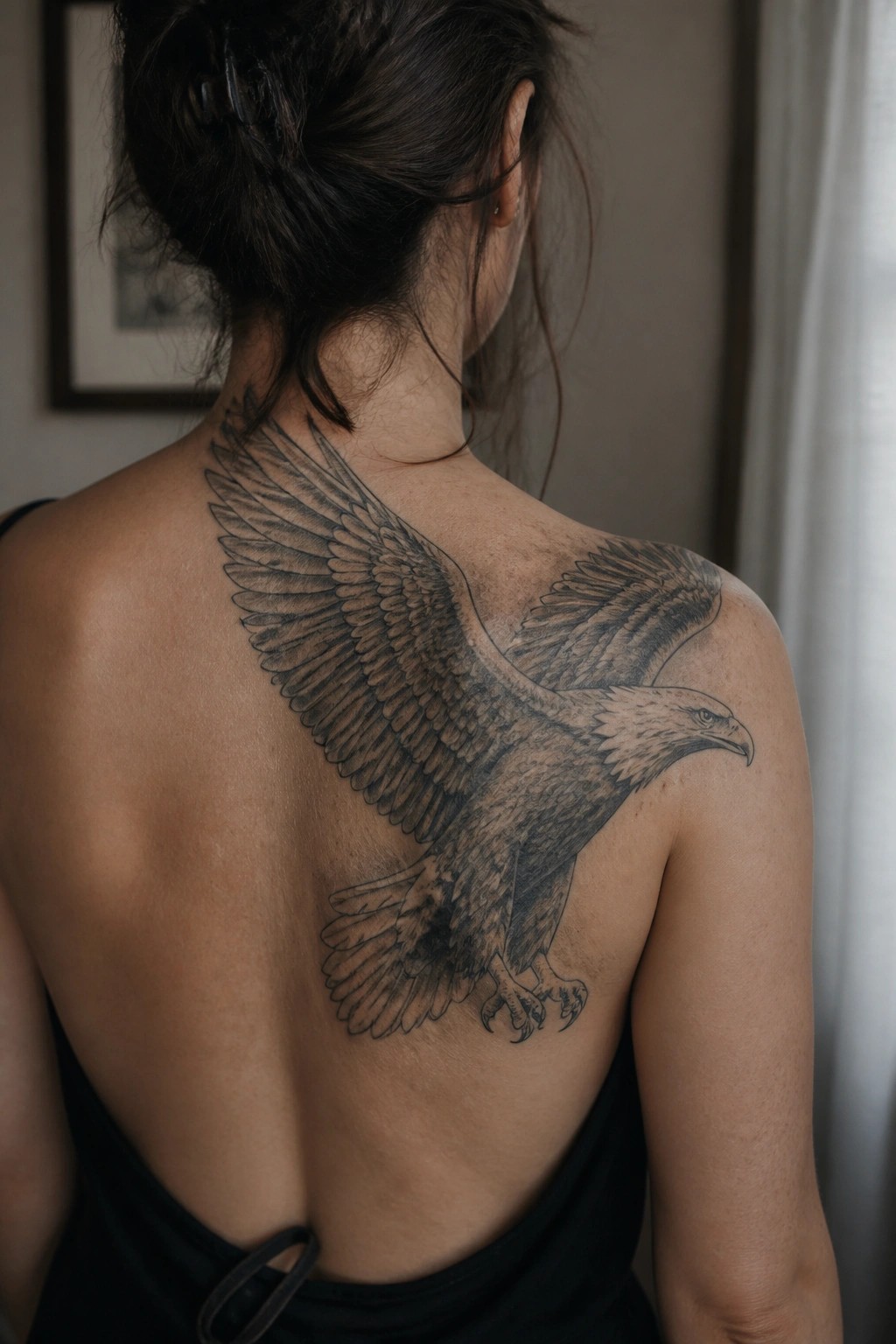 Woman with hair in bun shows large eagle tattoo on upper back and shoulder