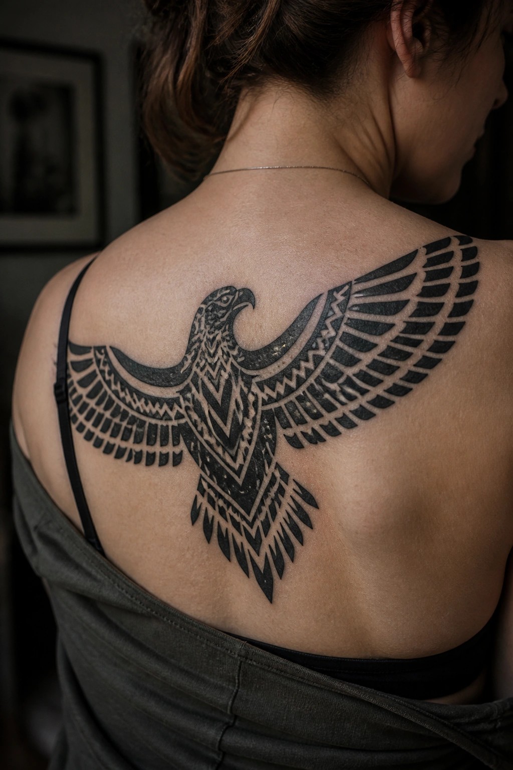 Woman with a large black tribal eagle tattoo across her upper back, wings spread wide in geometric patterns.