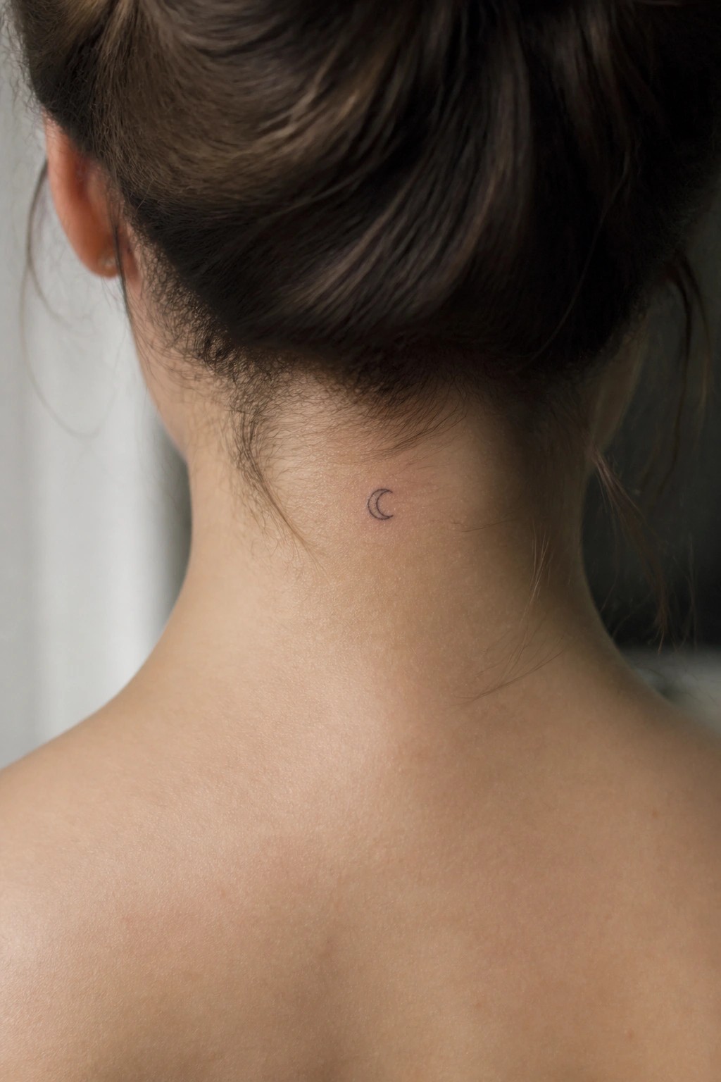 Small crescent moon tattoo on the back of a woman's neck