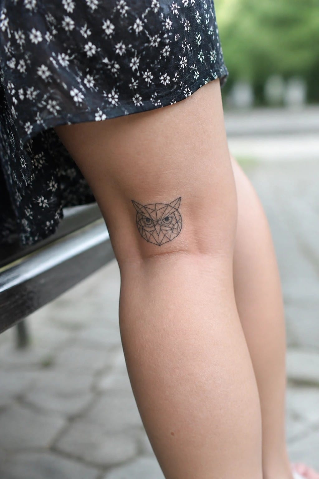 Geometric owl tattoo on knee under black floral dress hem.