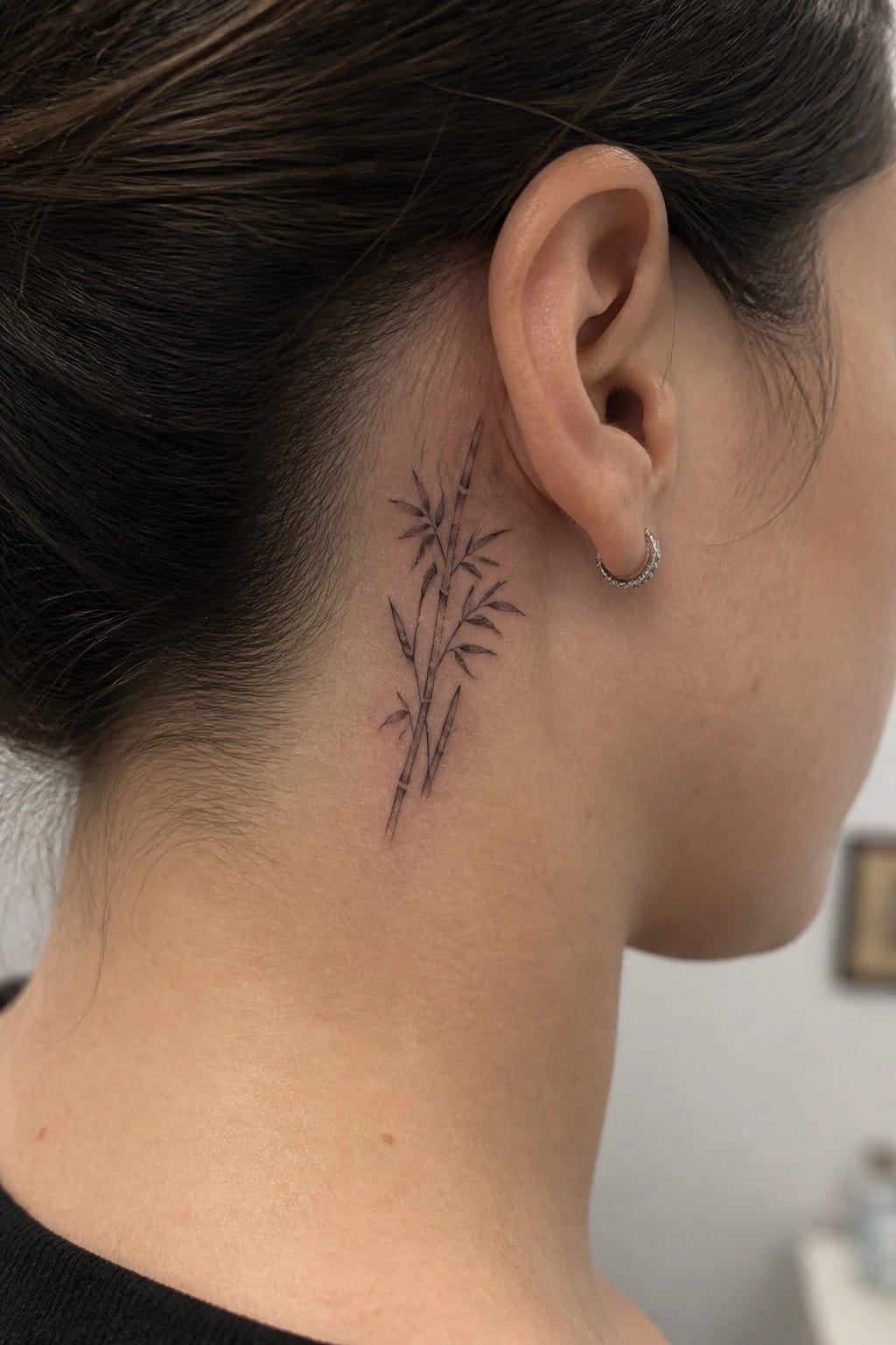 Black bamboo tattoo on neck behind ear with jeweled hoop earring and dark hair