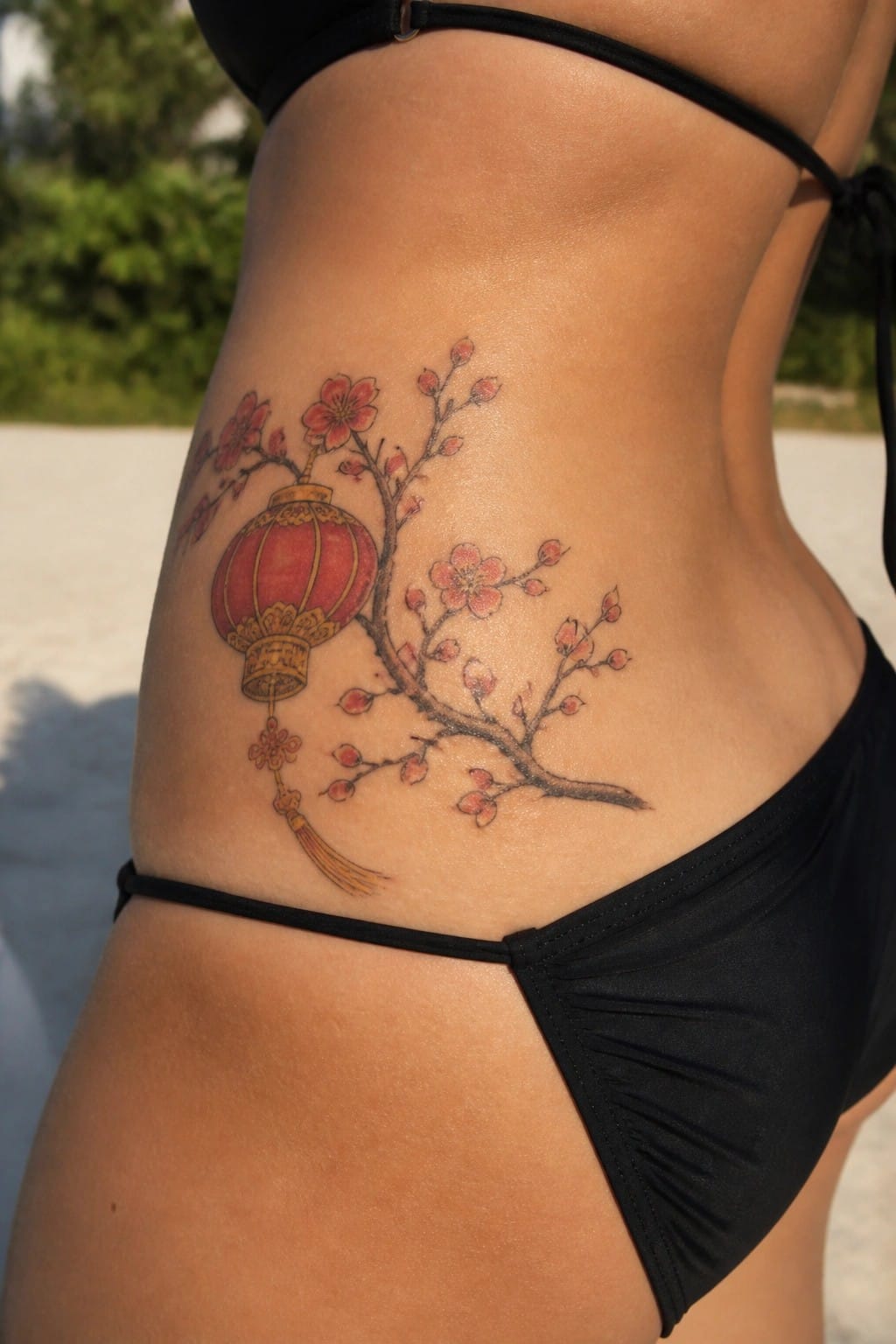 A tattoo of a red Chinese lantern and cherry blossom branches on the side of a torso.