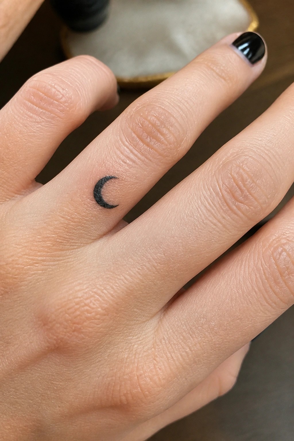 Fingers with small black crescent moon tattoo and glossy black nail polish
