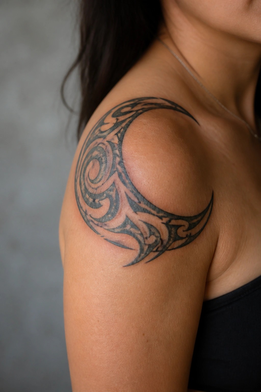 Shoulder with large black tribal swirl tattoo, black top, thin necklace