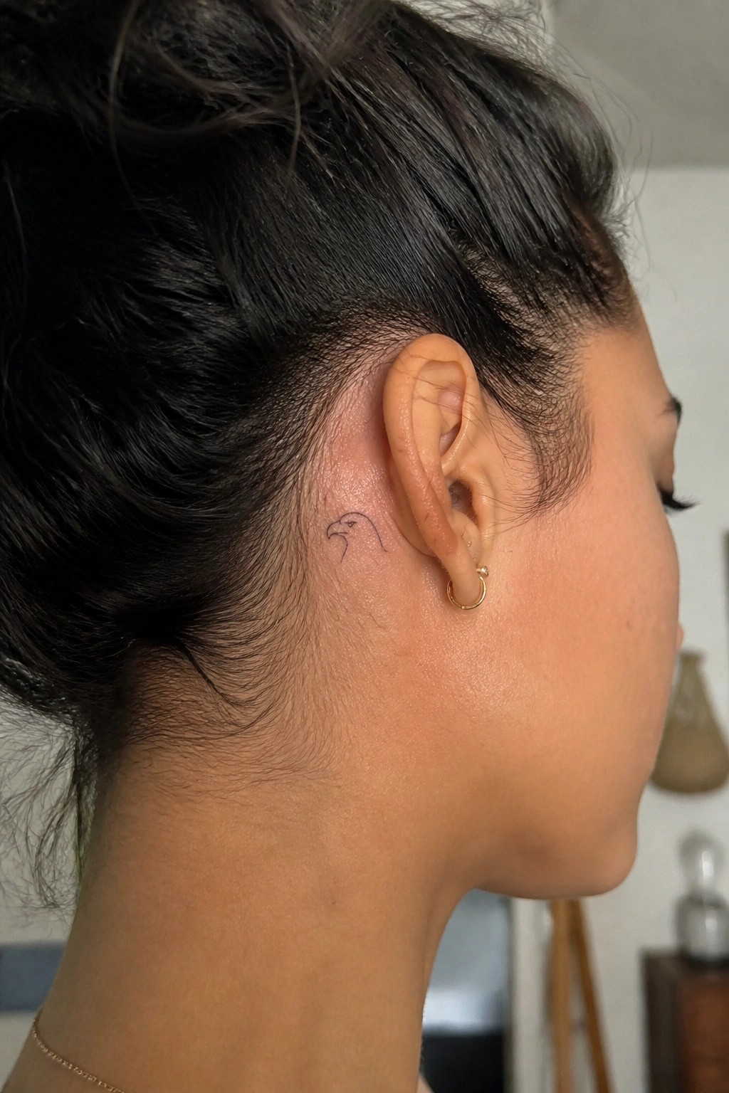 Small fine line eagle head tattoo placed behind a woman's ear on short cropped hair.