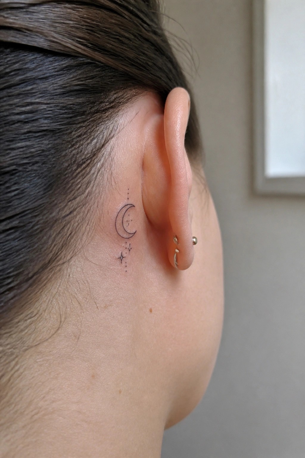 Close-up of ear with crescent moon and stars tattoo plus small hoop earring
