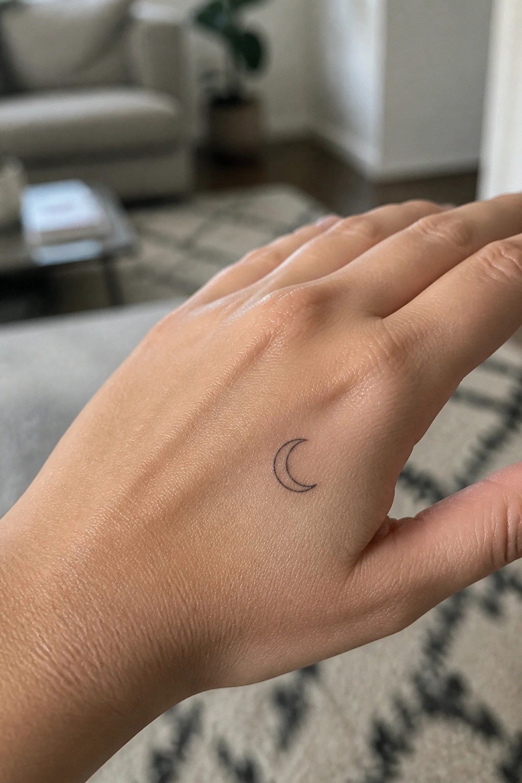 Small crescent moon tattoo on the back of a hand in minimal black line style