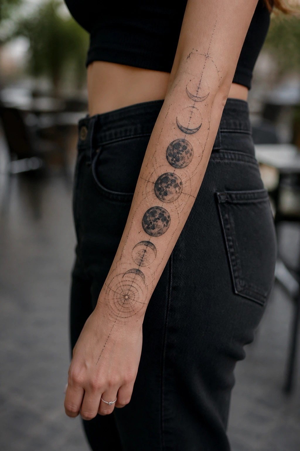 Arm with moon phases tattoo on person in black crop top and jeans.