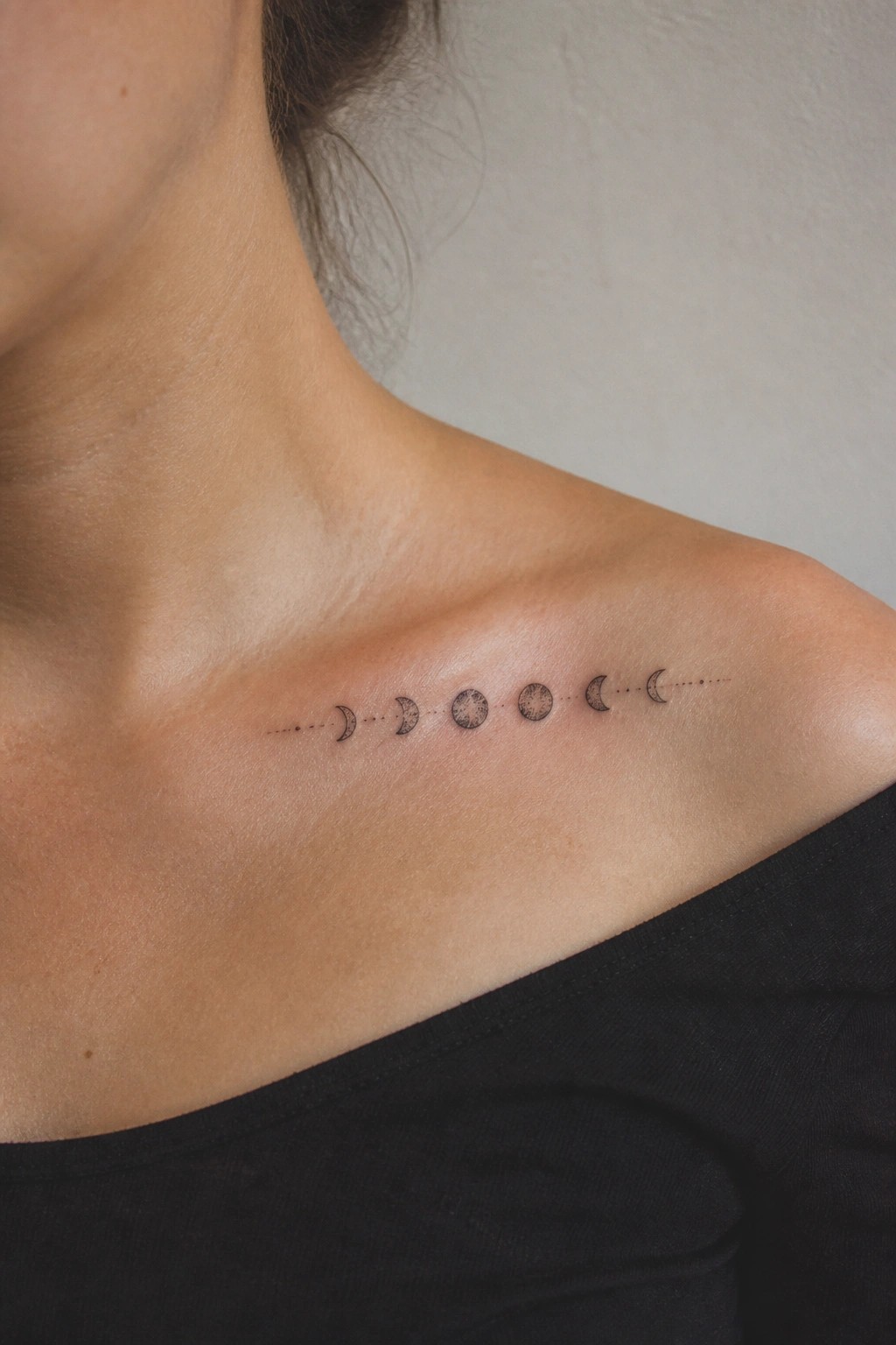 Moon phase tattoo on light skin above black top on shoulder.