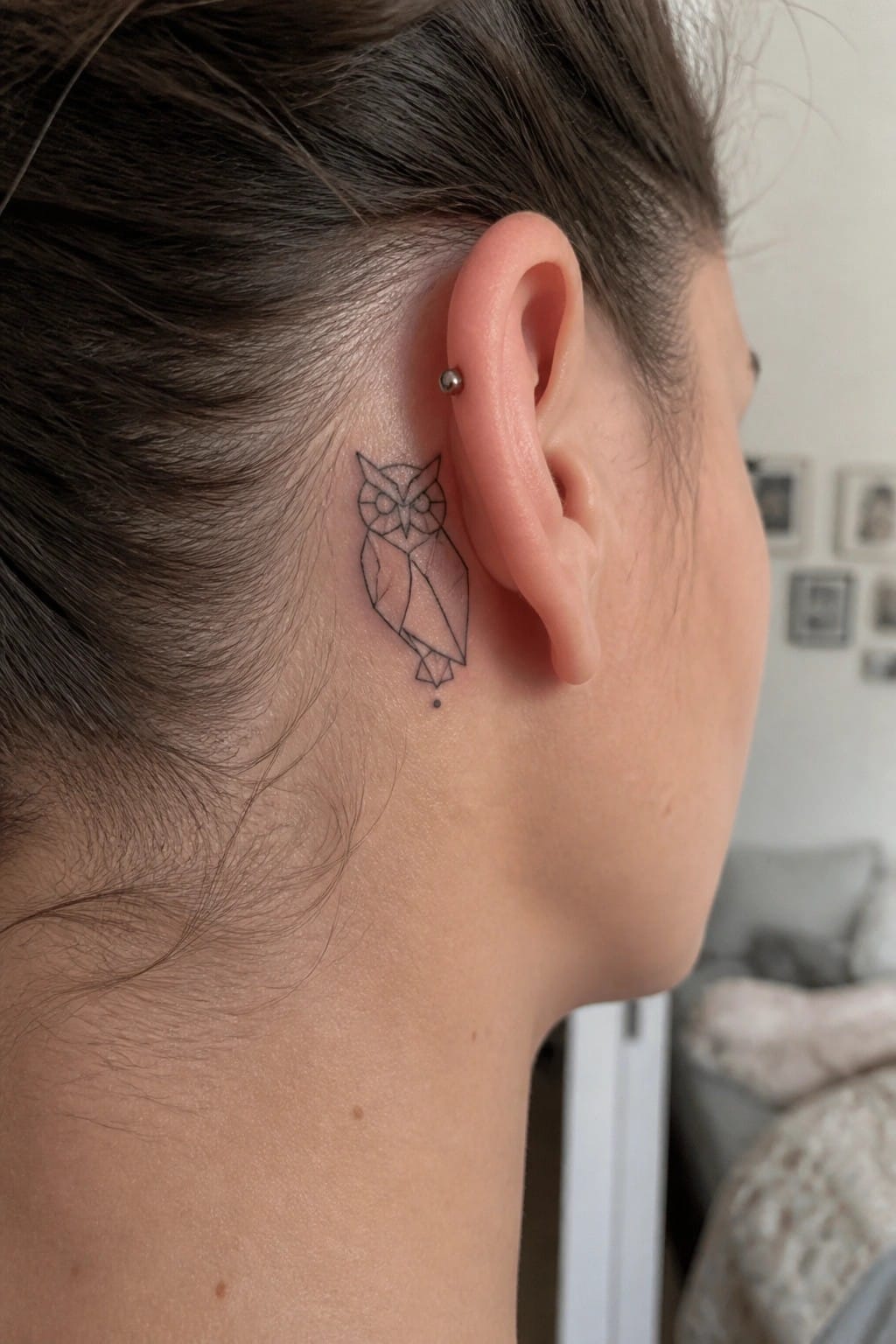 Geometric owl tattoo behind ear with small stud earring and dot