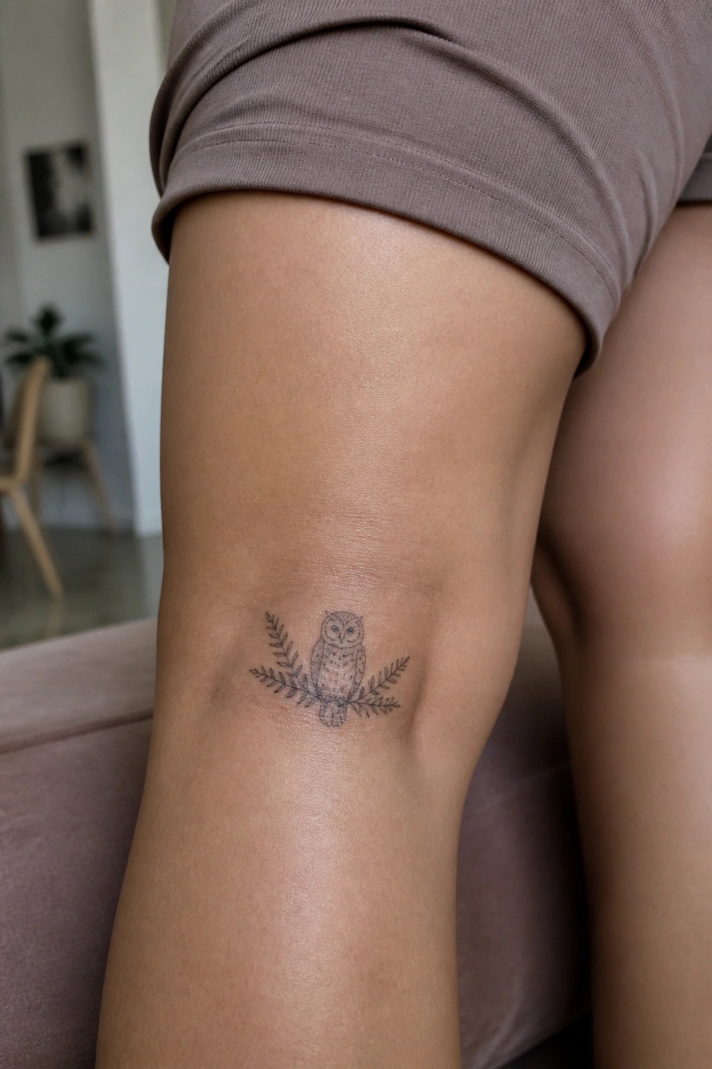 Owl tattoo on thigh beneath mauve shorts with leafy branch design.