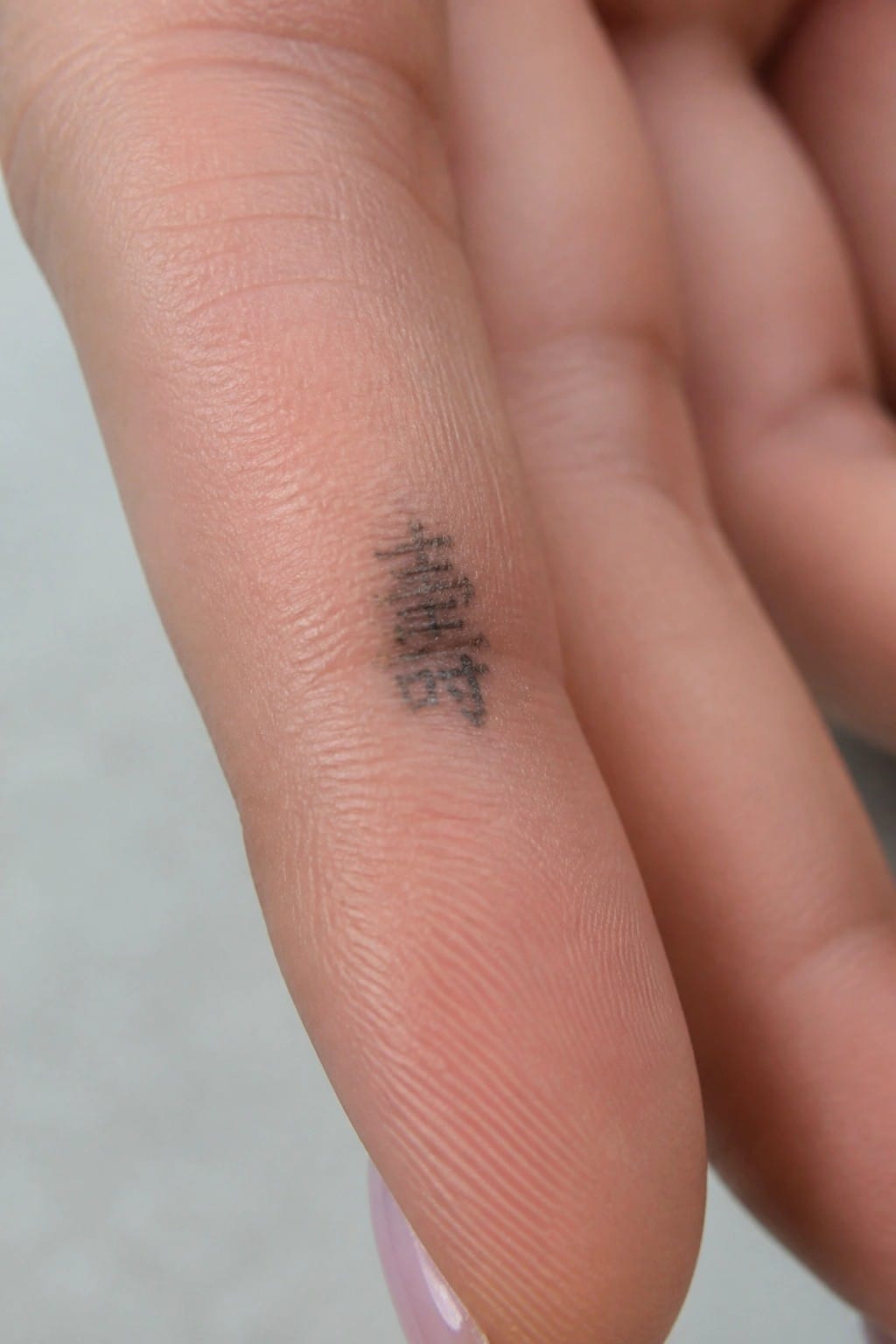 Close-up of light-skinned finger with small vertical black character tattoo.