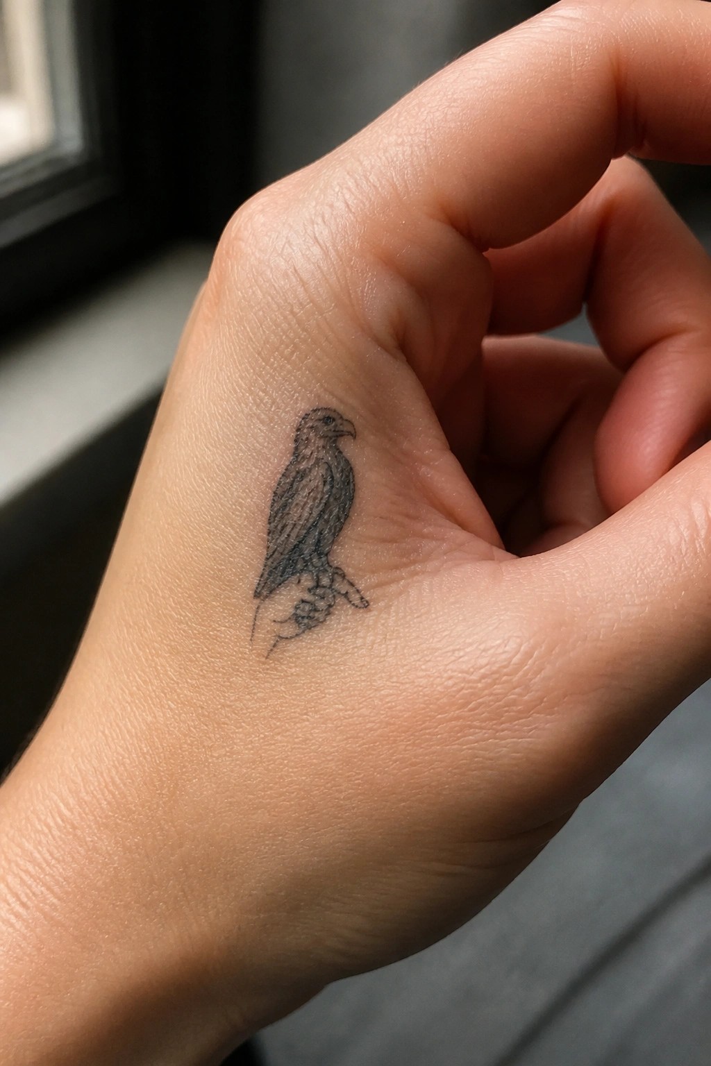 Small black hawk tattoo on the back of a light-skinned hand