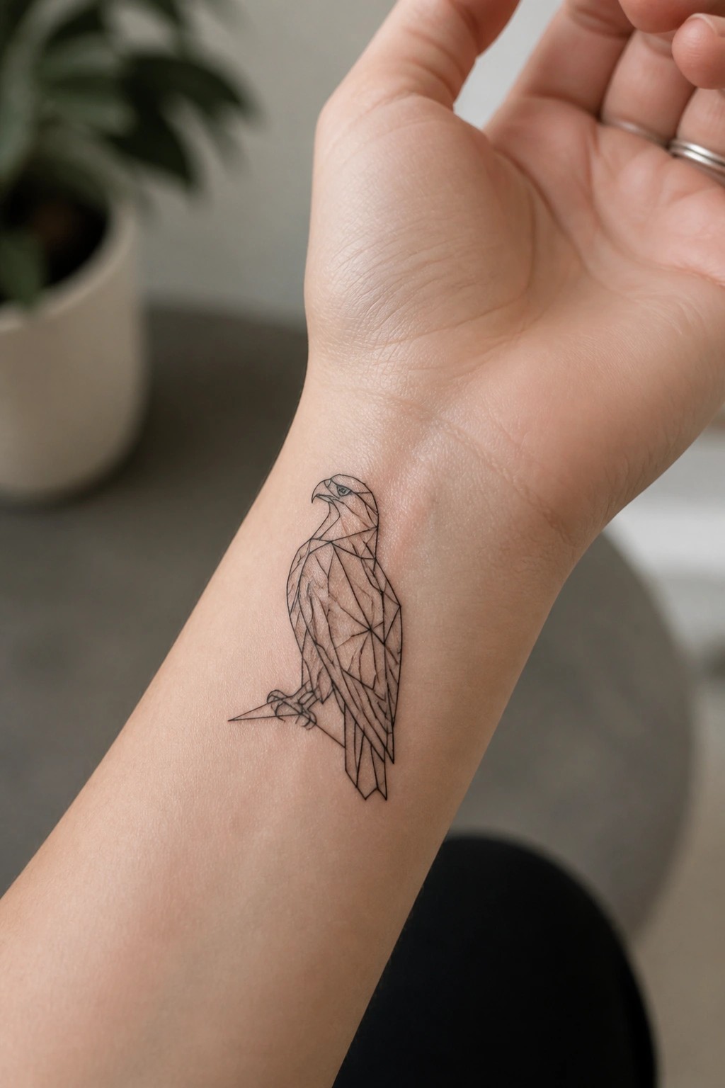A small geometric line tattoo of a perched eagle on the inner wrist.
