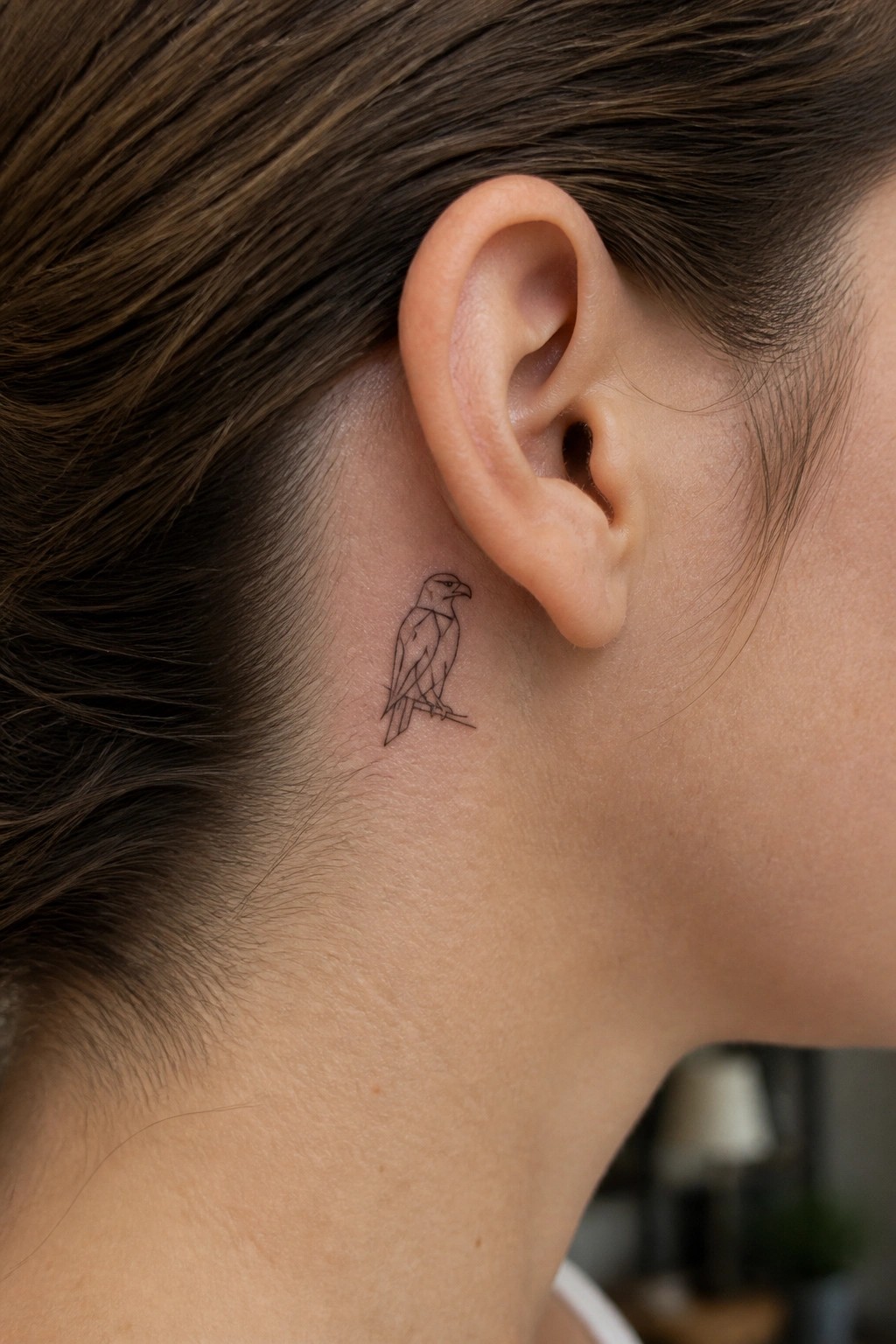 Small line drawing of a perched eagle tattoo placed behind a woman's ear on the neck