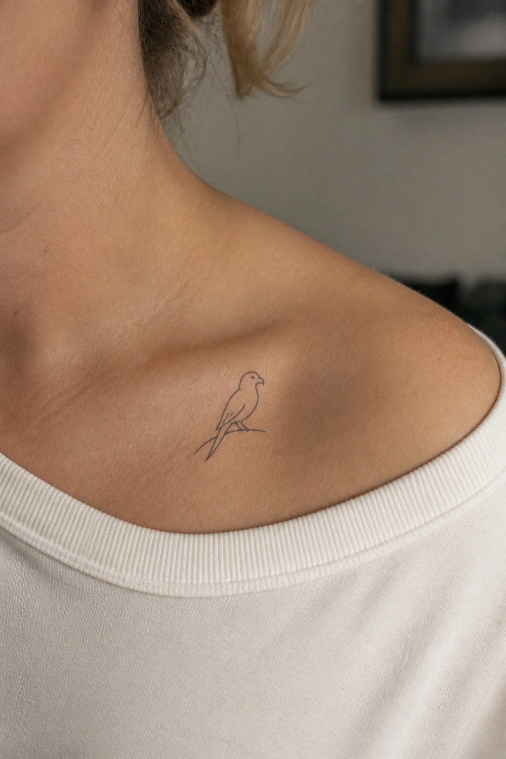 Minimalist bird line tattoo on shoulder above white off-shoulder top