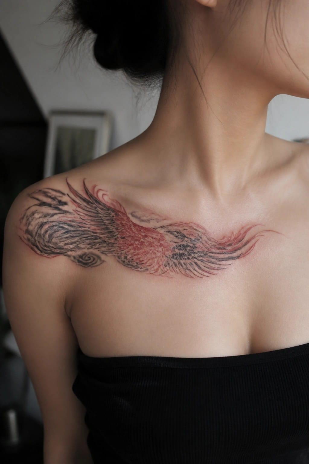 Large red-and-black wing tattoo across woman's shoulders above black strapless top