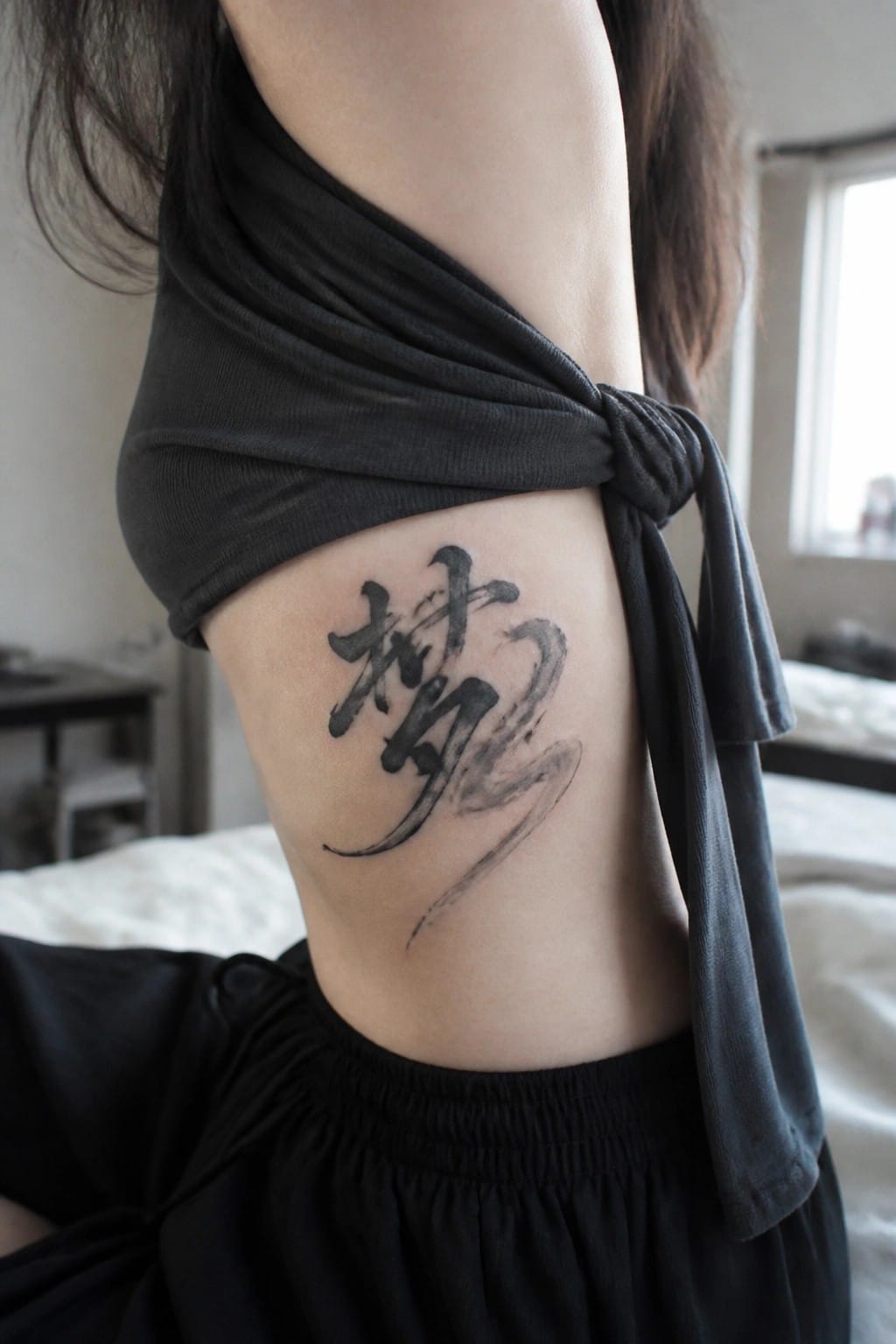 Black brushstroke tattoo on side torso beneath knotted black sleeveless top