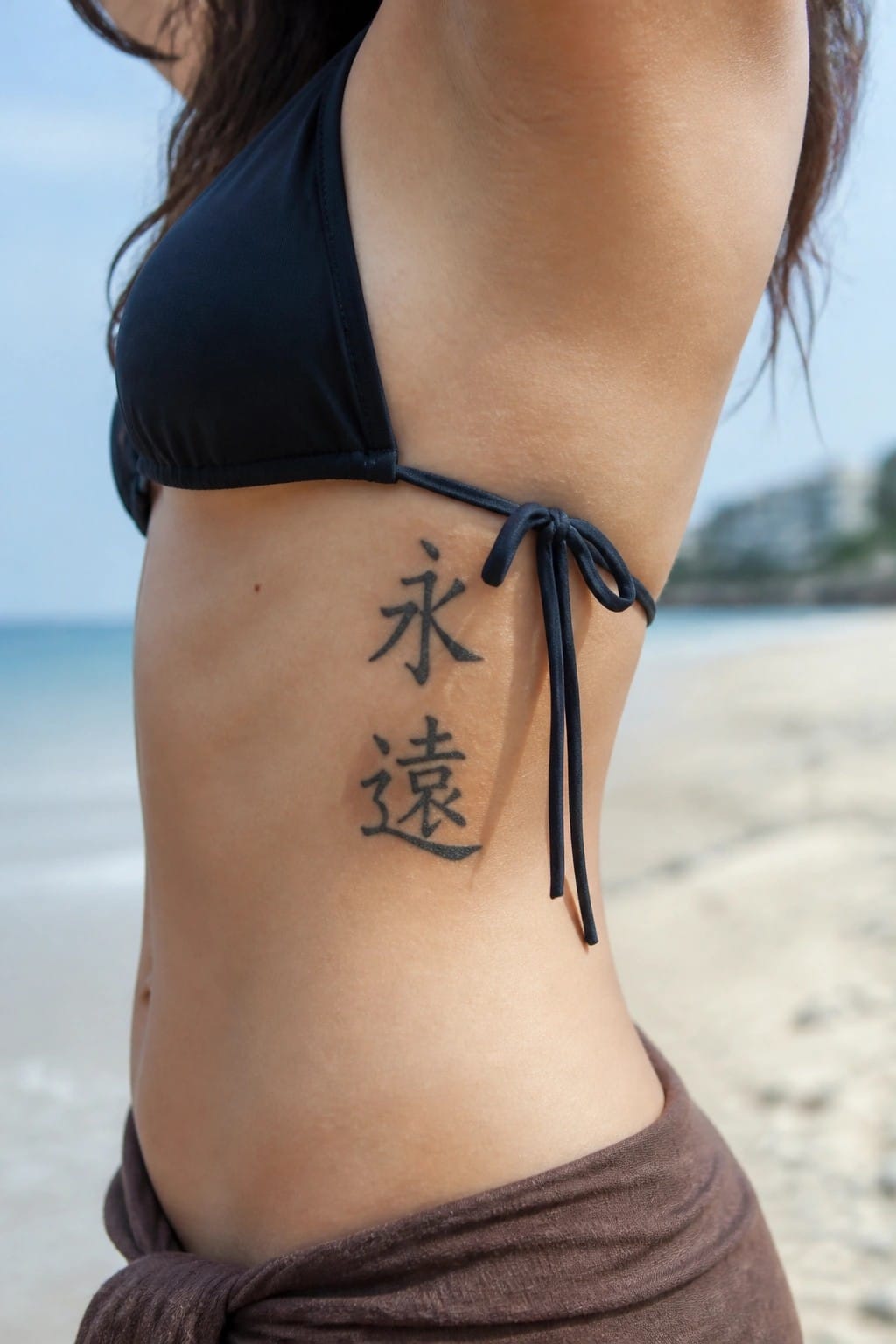 Woman's side torso with Chinese tattoo, black bikini tie, beach background