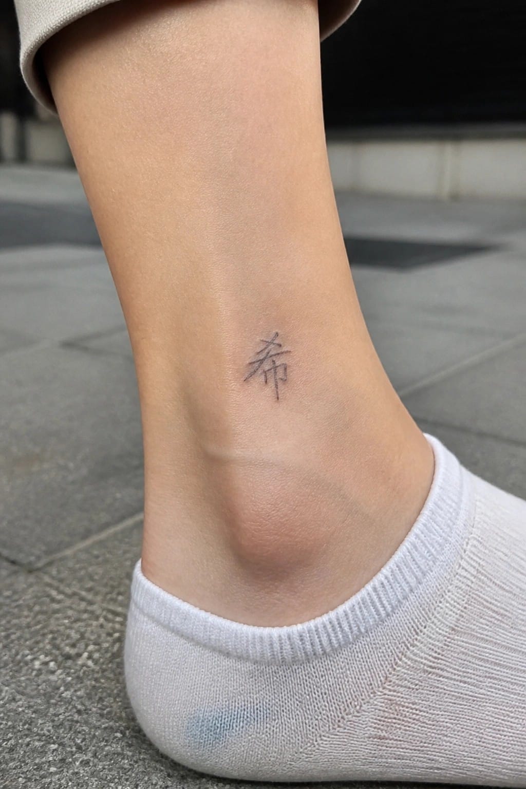 Small black Chinese character tattoo on ankle above white sock and beige cuff