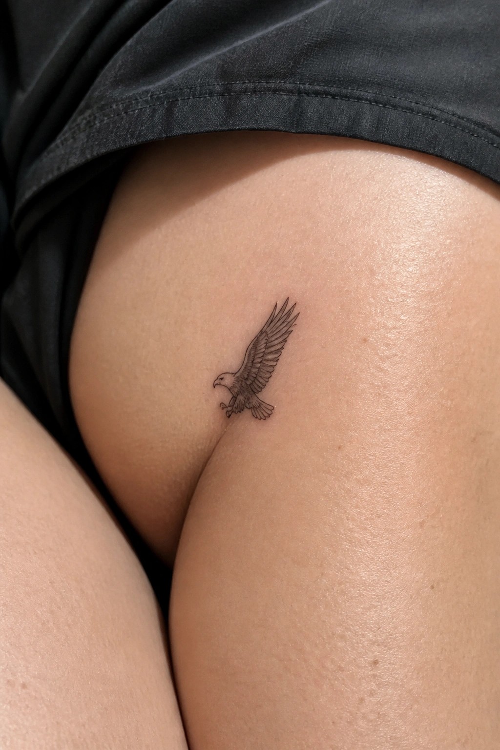 Small black eagle tattoo on upper thigh beneath black shorts.