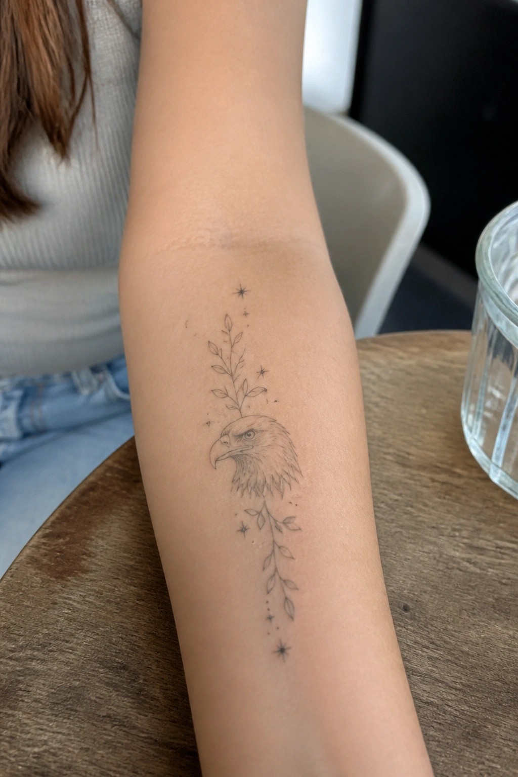 Fine line eagle head tattoo with leaves and stars on forearm