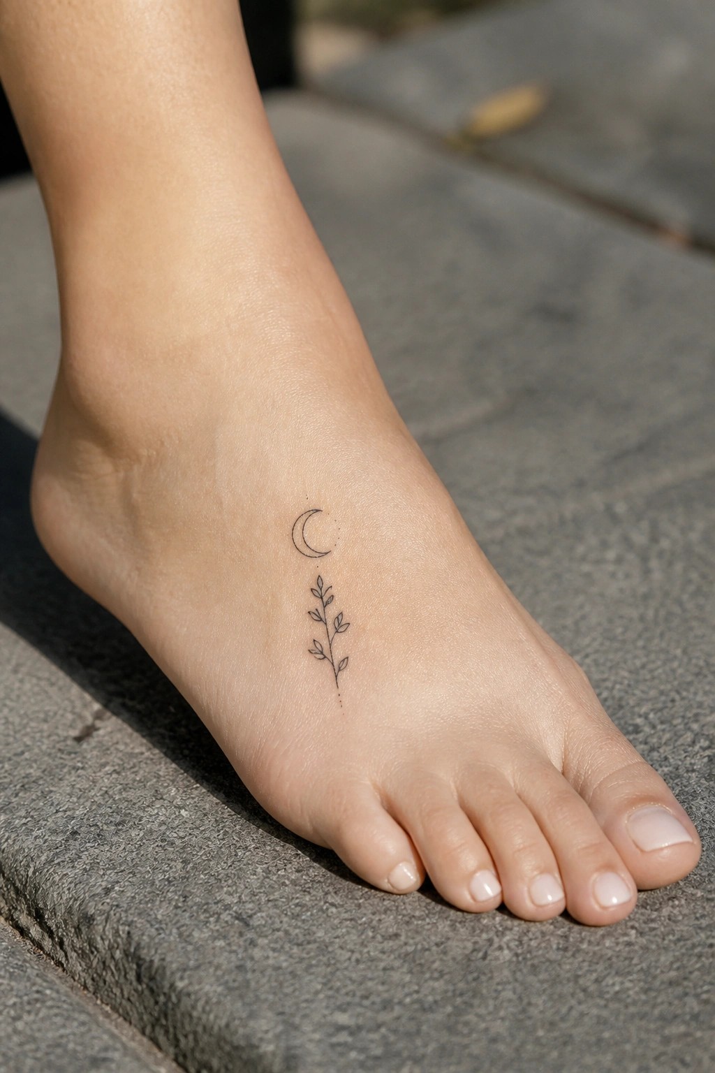 Bare foot on gray stone with crescent moon and leafy branch tattoo