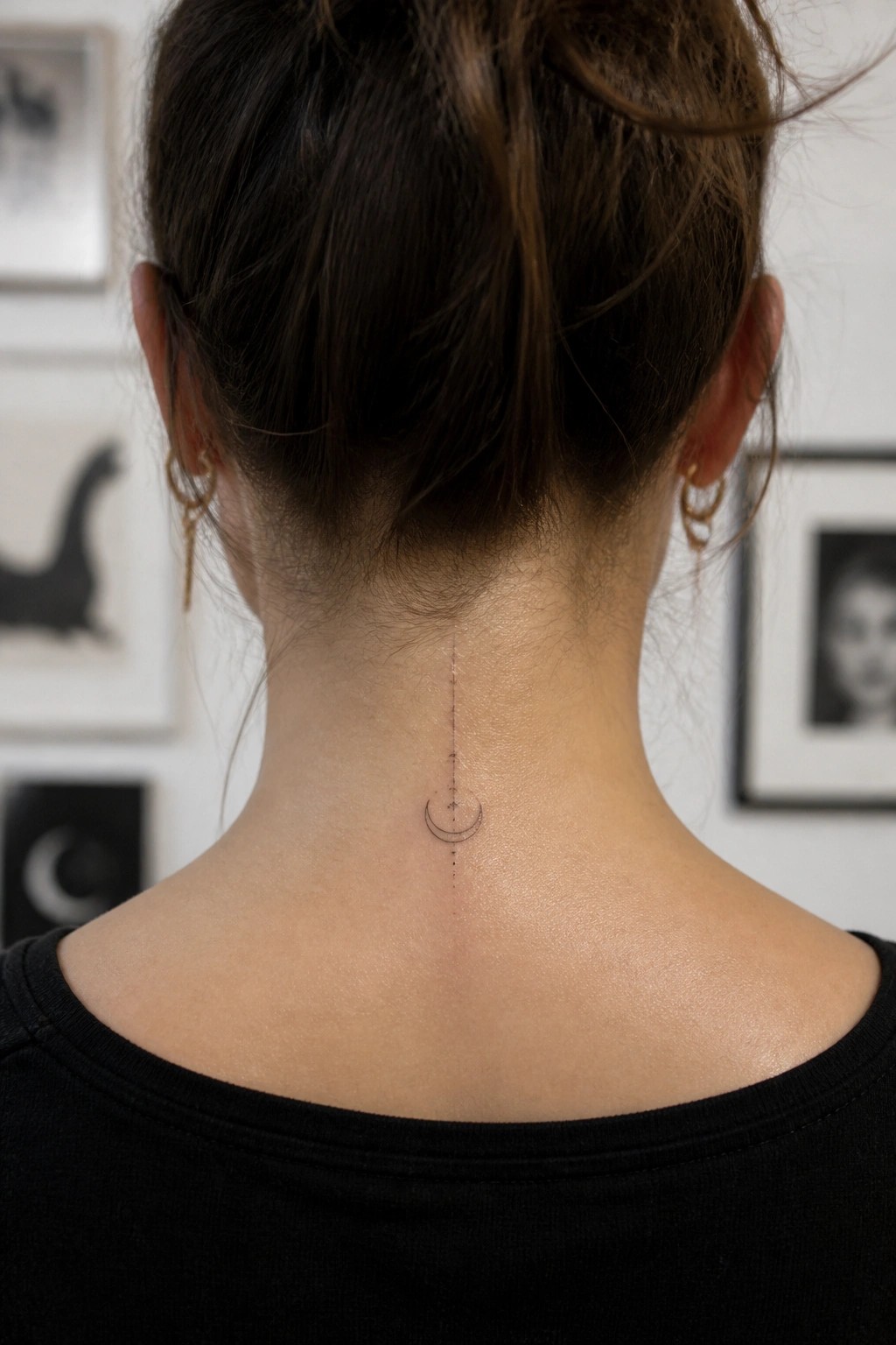Fine line crescent moon tattoo with a vertical dotted line centered on the back of a woman's neck