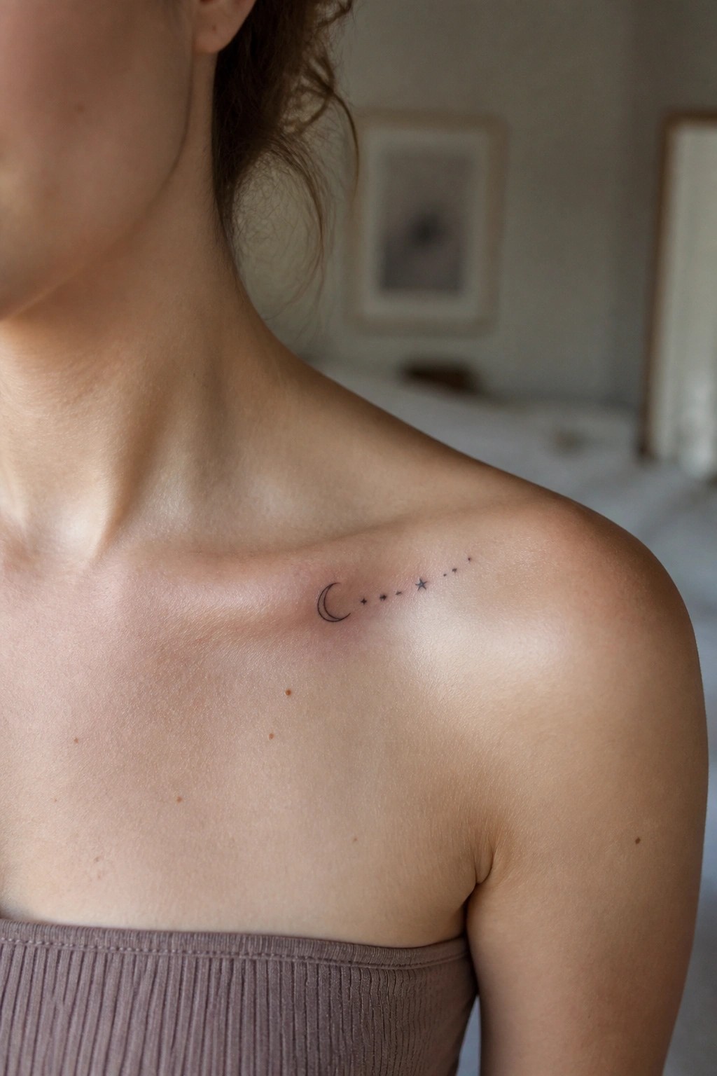 Crescent moon and stars tattoo on woman's shoulder above mauve strapless top