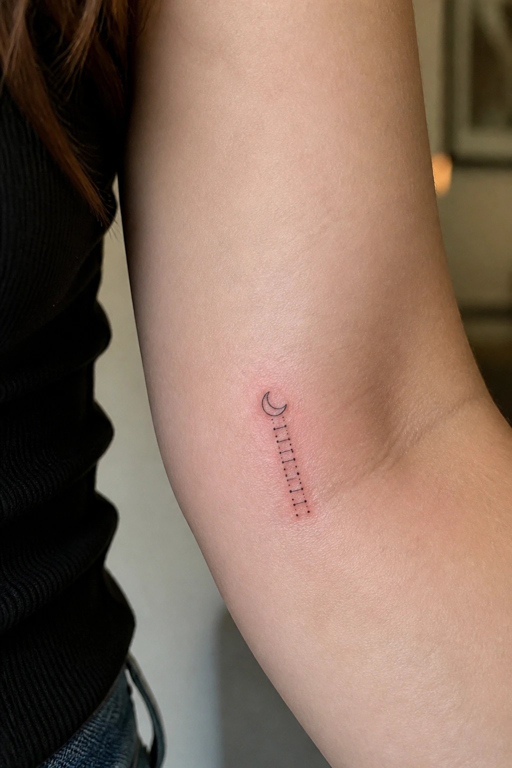 Small fine line tattoo of a crescent moon above a vertical row of dots on the inner forearm