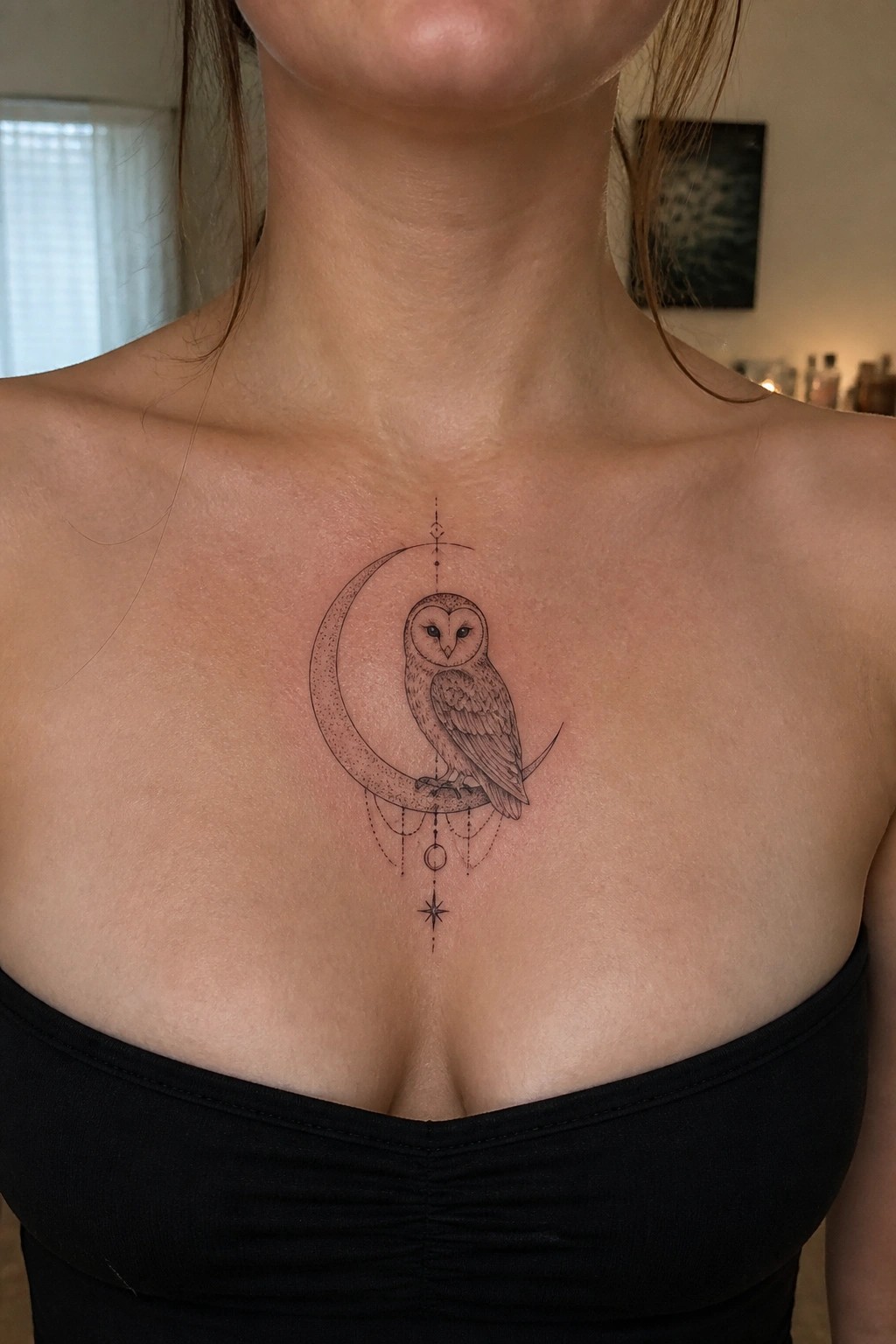 Fine line tattoo of an owl perched on a crescent moon with celestial accents on a woman's upper chest