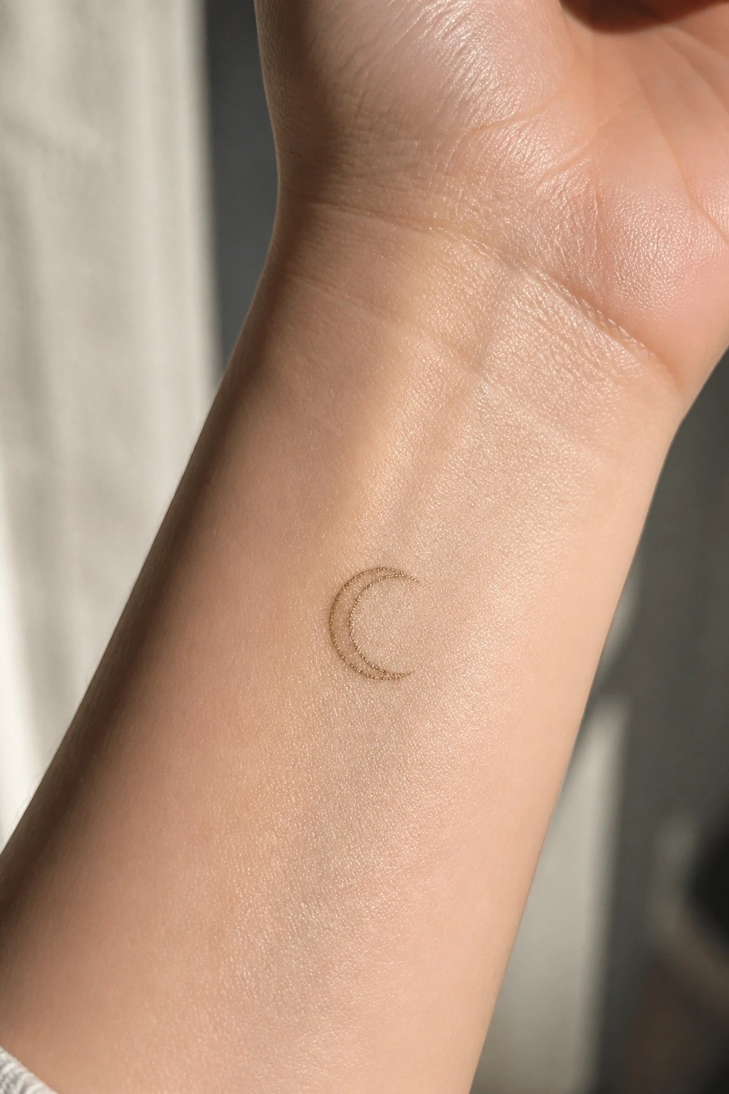 Small crescent moon tattoo with a dotted outline on the inner wrist
