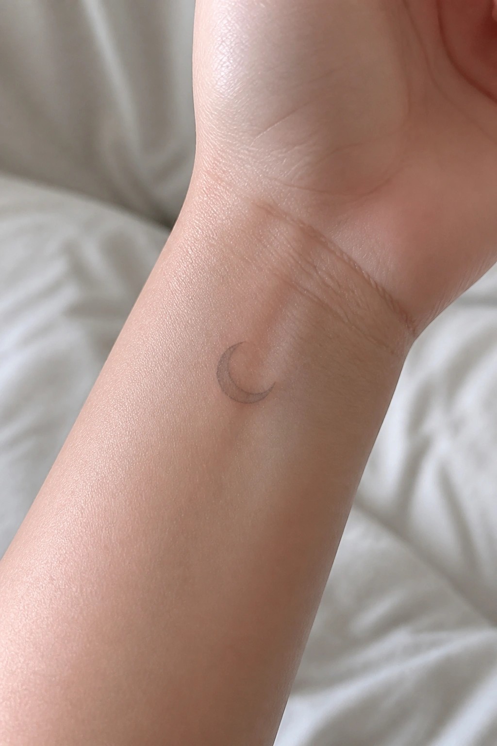 Small crescent moon tattoo in thin outline style on the inner wrist