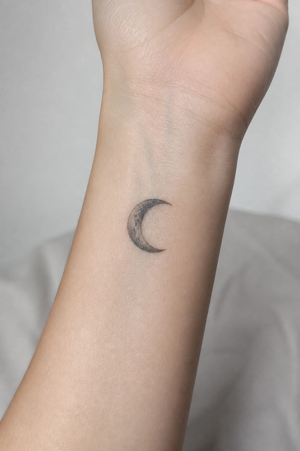 Small shaded crescent moon tattoo on the inner wrist
