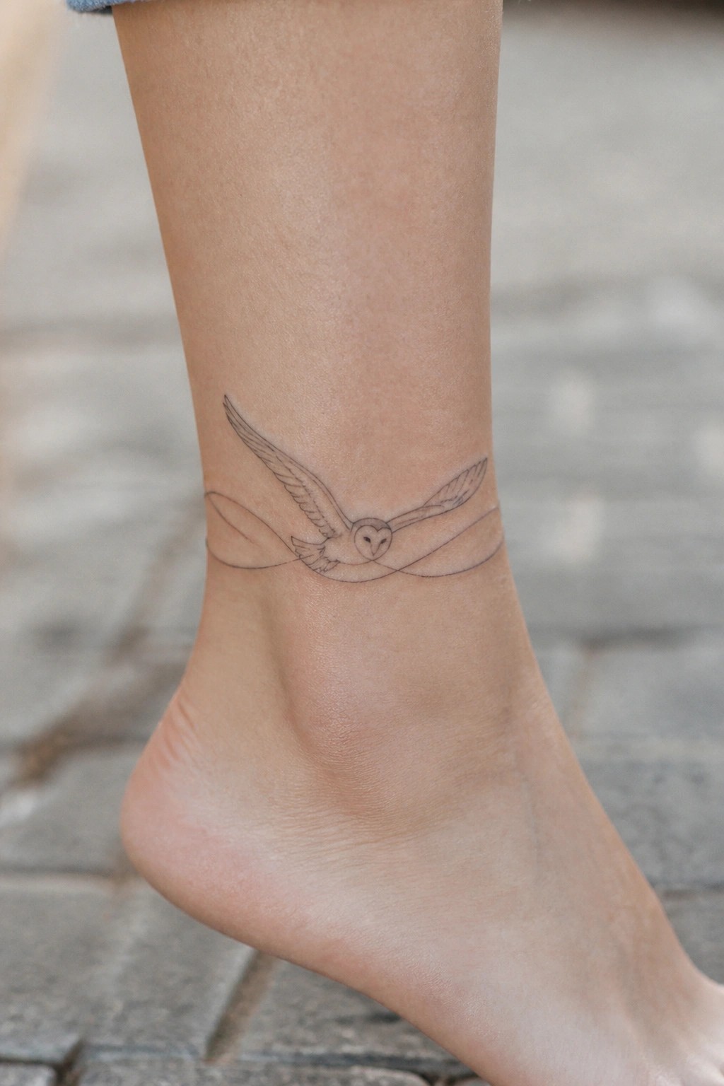 Owl tattoo with outstretched wings on light-skinned ankle above bare foot