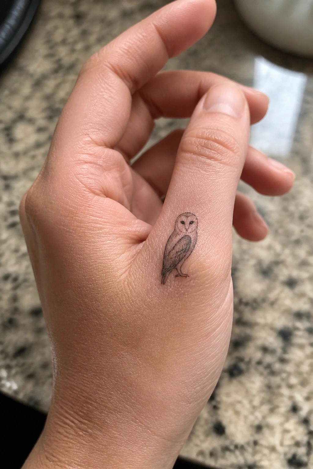 Small barn owl tattoo in fine line black and grey on the side of an index finger