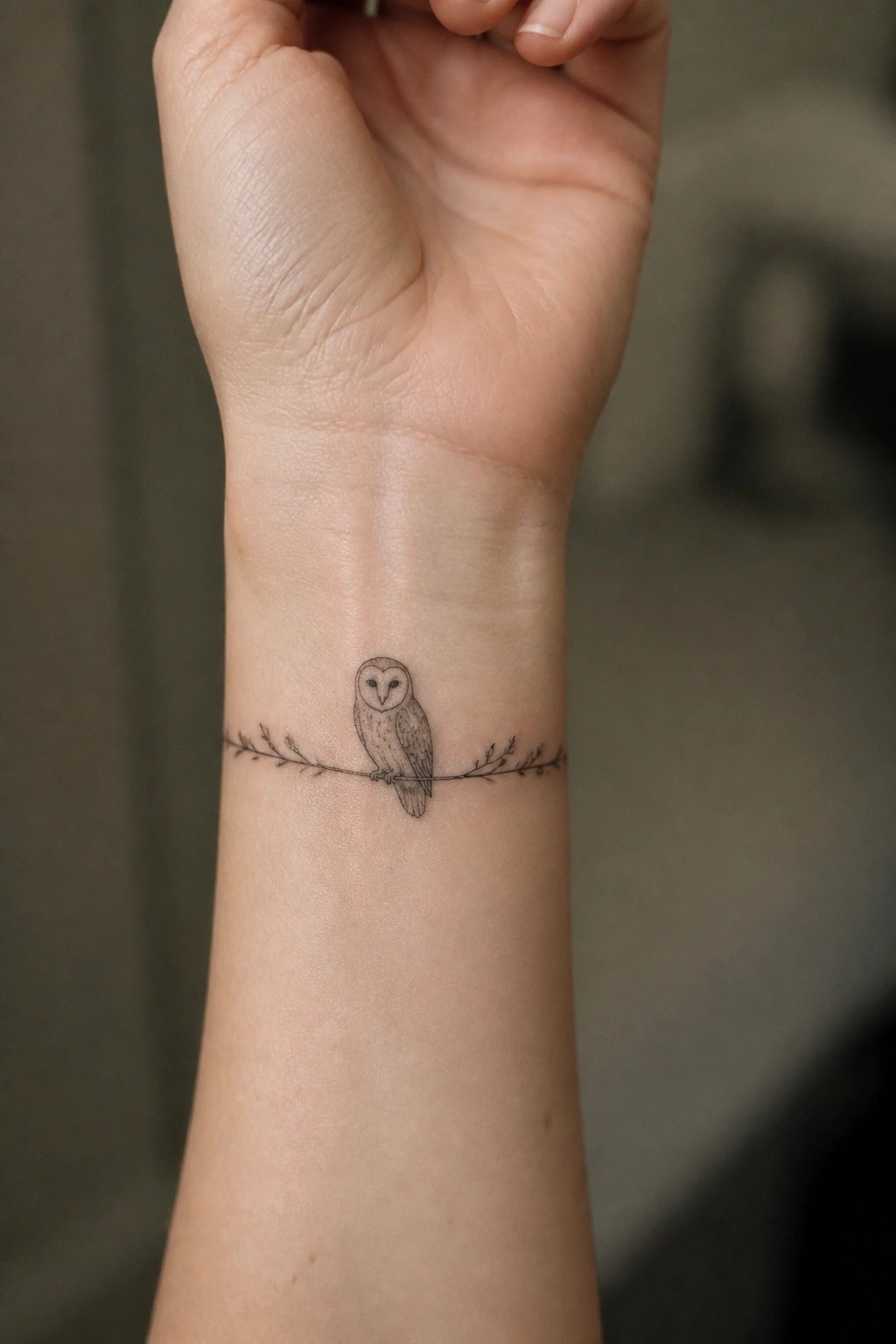 Fine-line owl tattoo on wrist perched on leafy branch