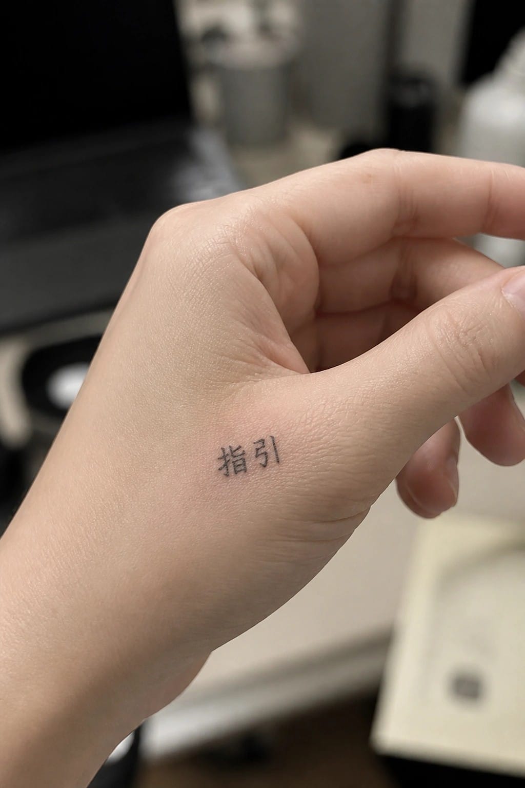 Light-skinned hand with black Chinese characters tattoo near thumb base.