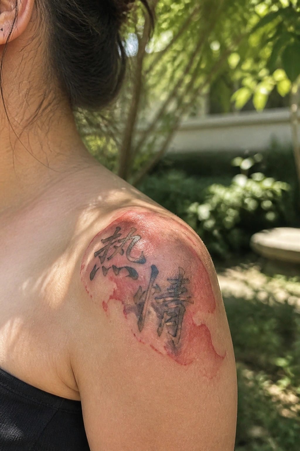 Fresh Chinese character tattoo on red inflamed shoulder skin in sunlight