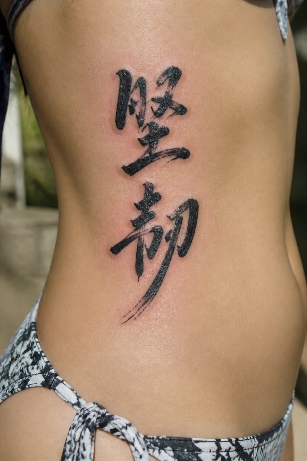 Black Chinese calligraphy tattoo on reddened skin above patterned bikini bottom