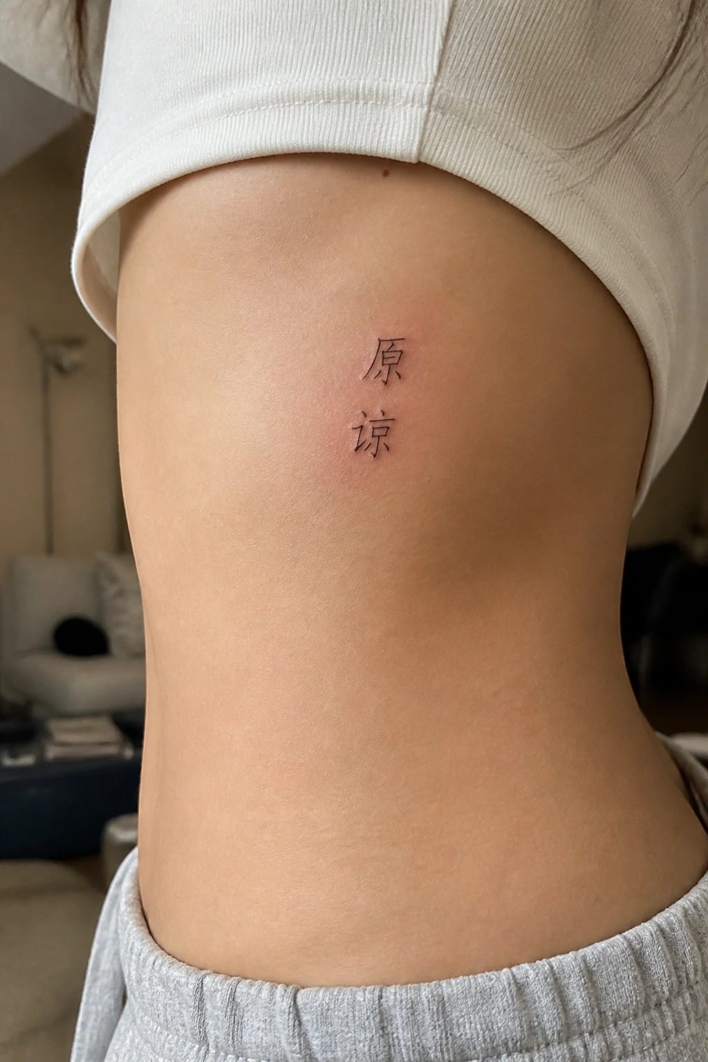 Small black Chinese characters tattooed vertically on the side of a torso in fine line style